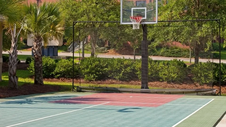 Clean outdoor basketball court with a bright red or blue painted surface, clear white boundary lines, and an intact net, ready for street play.