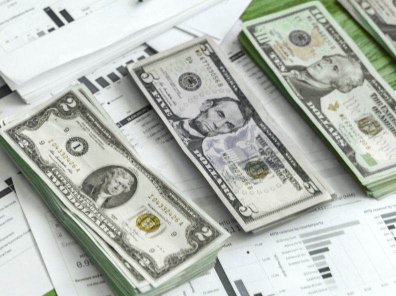Stacks of twenty and fifty dollar bills on papers with charts and graphs.