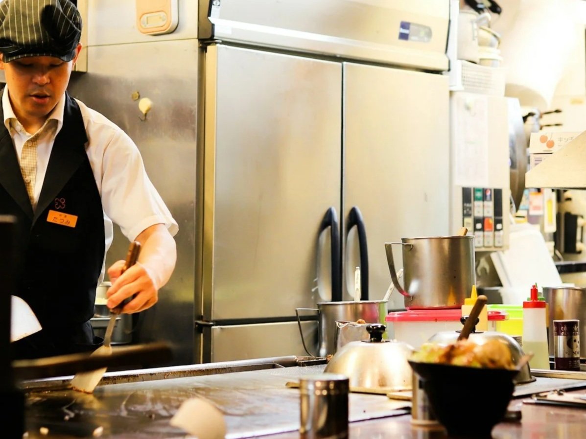 A chef cooking on a teppanyaki grill in a restaurant kitchen, with various cooking utensils and ingredients on the counter.