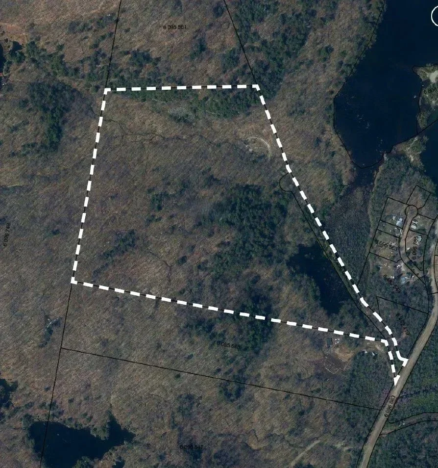 A satellite map of a wooded area with a dashed white line outlining a specific property boundary.