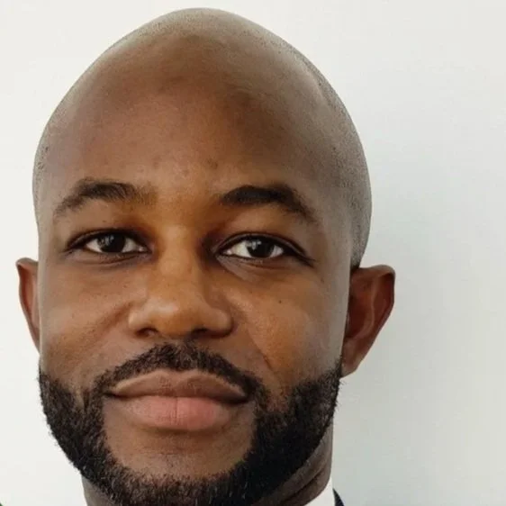 Close-up of  Ian Corbin with a bald head, dark beard, and mustache, looking directly at the camera with a neutral expression against a plain light background.