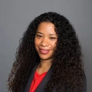 Portrait of Dr. Angela Randolph with long, curly black hair wearing a red top and dark blazer, smiling against a gray background.