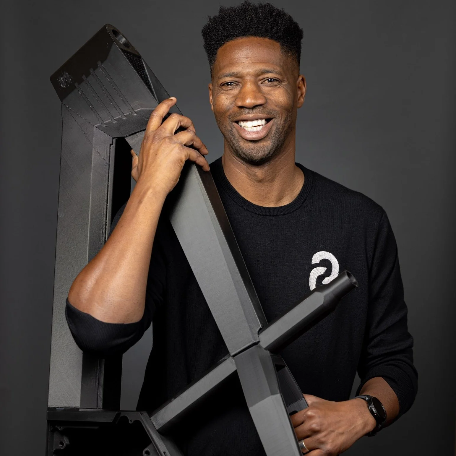 Brandale Randolph smiling, holding a large electronic bike frame against his shoulder, in a studio with a dark background.