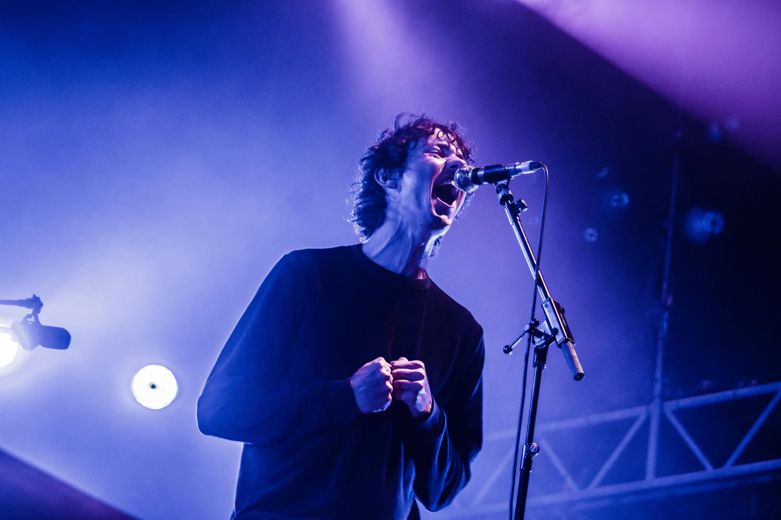 A man passionately singing into a microphone on stage with purple and blue lighting.
