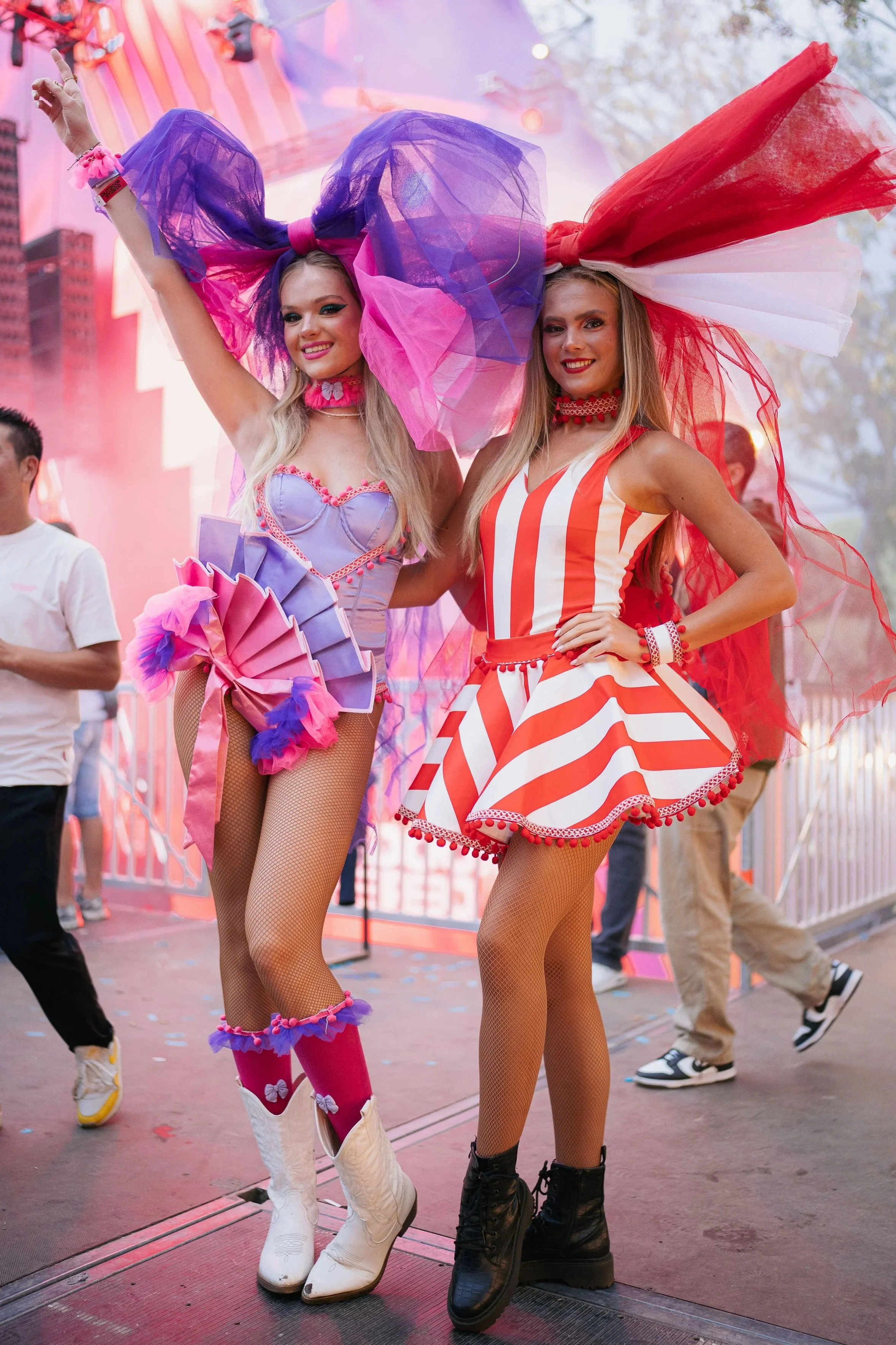 Two women dressed in colorful, playful costumes posing at an amusement park or carnival.