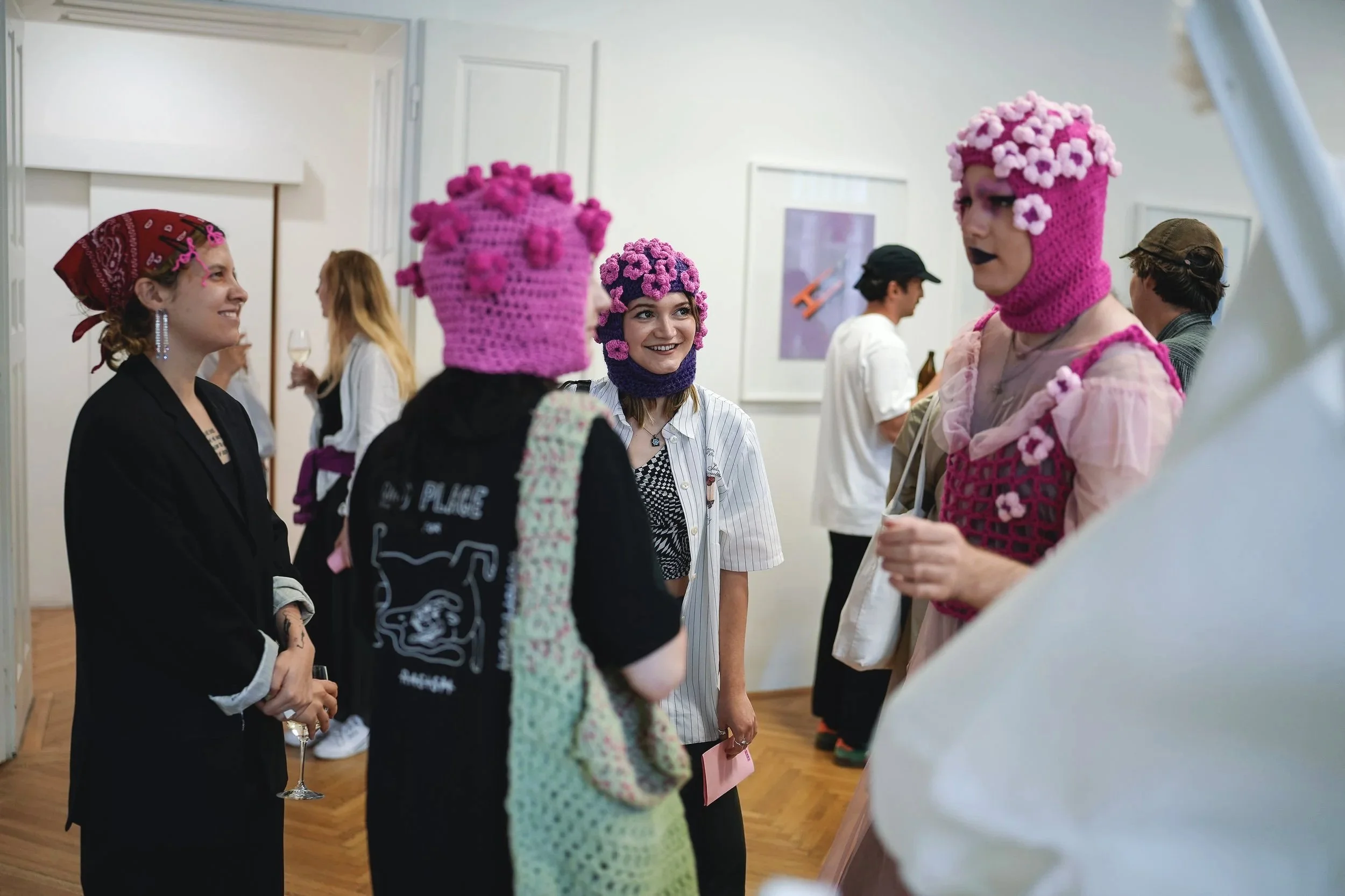 People at an art gallery wearing colorful knitted hats and accessories.