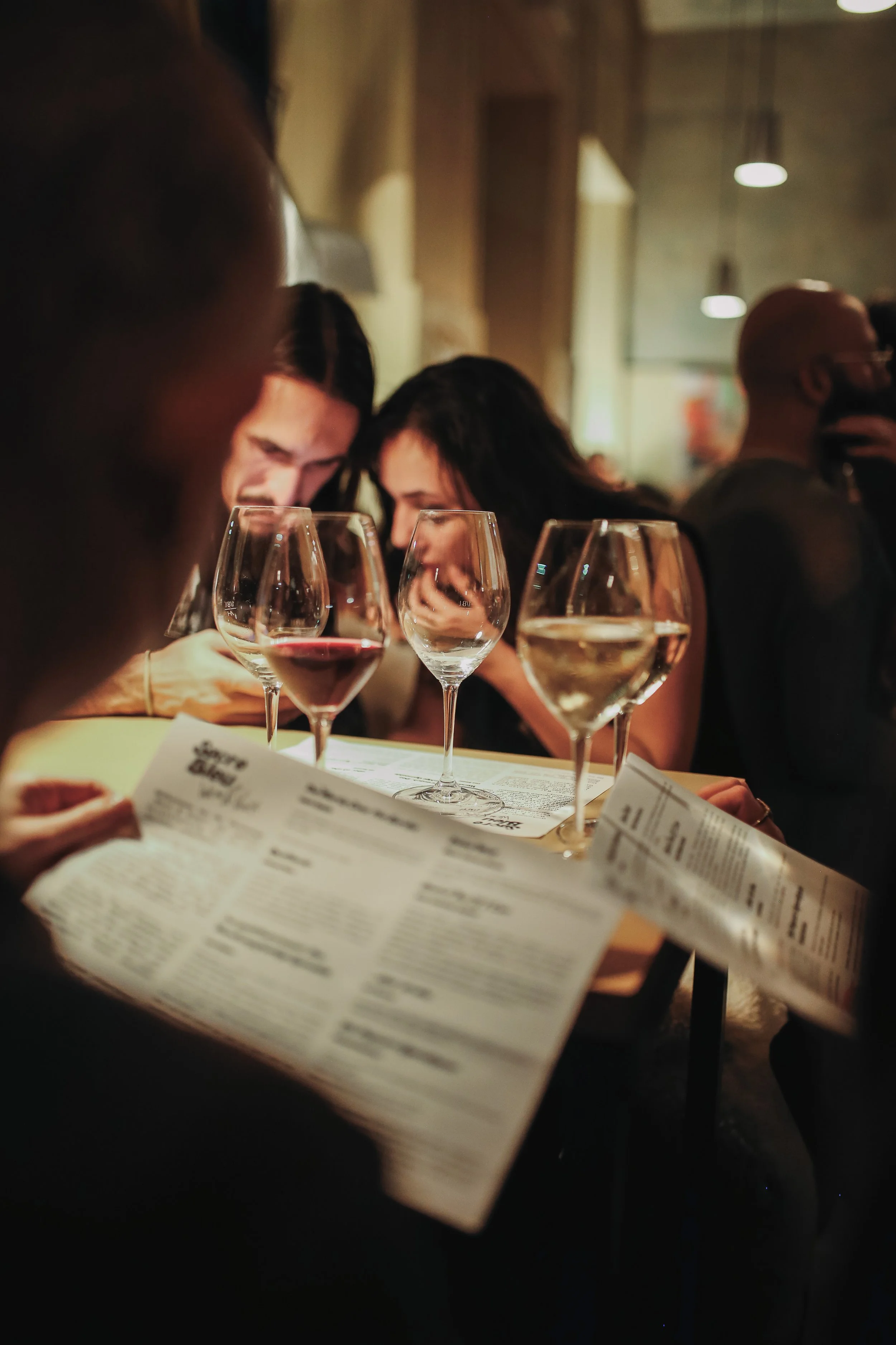People sitting at a table in a dimly lit restaurant, looking at menus with glasses of wine on the table.
