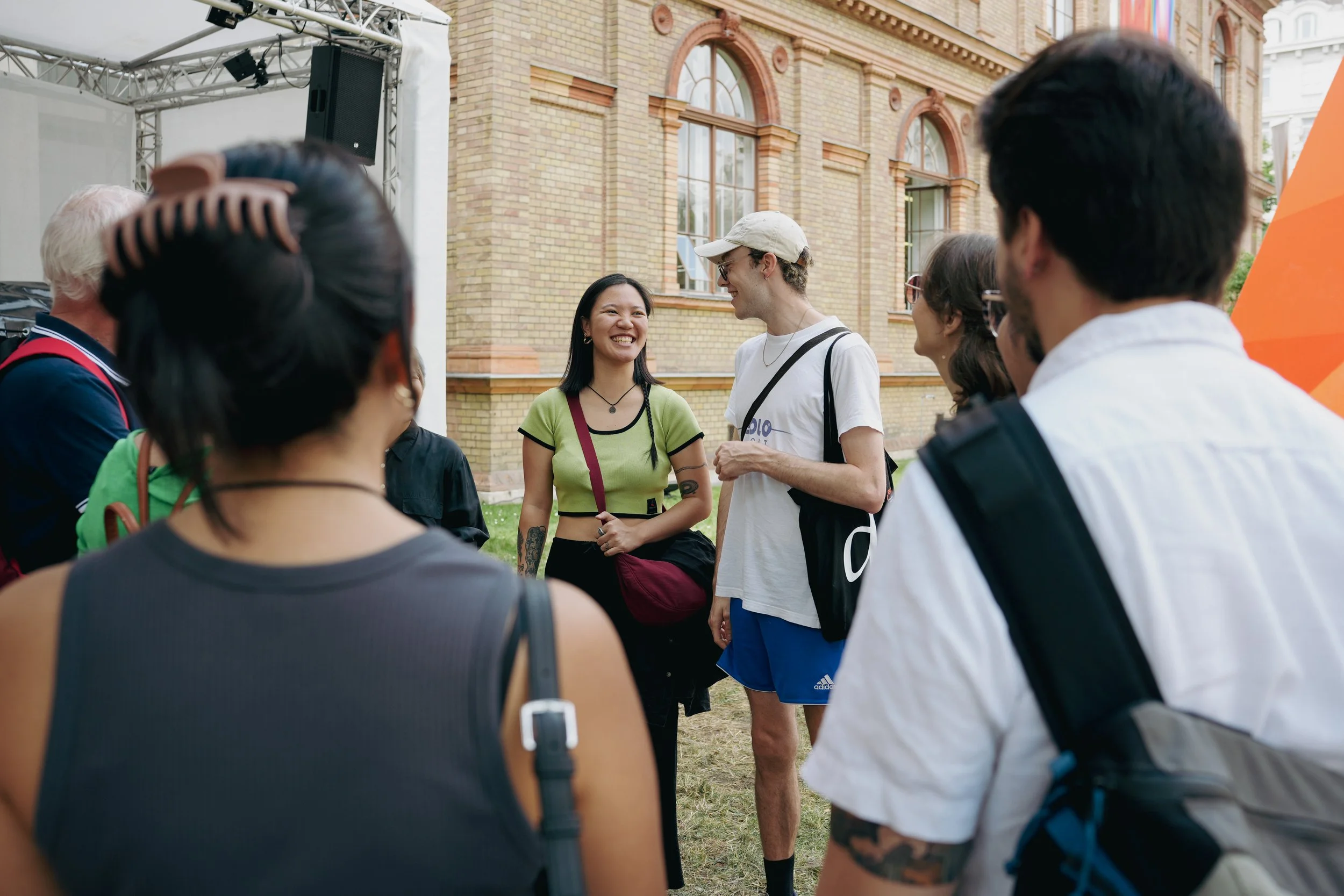 Group of people outdoors, engaging in conversation, with a brick building in the background.
