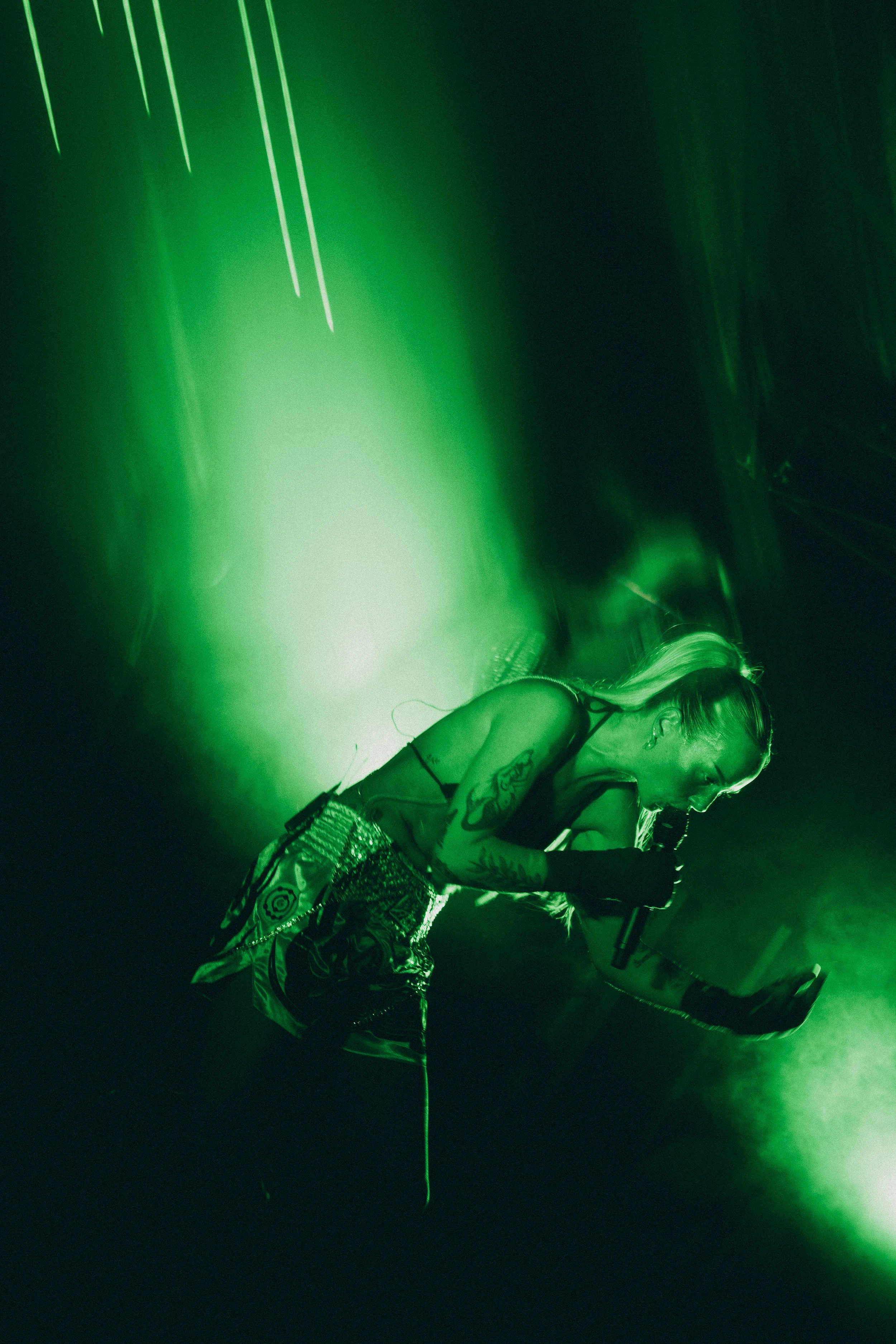 Performer singing into a microphone on stage bathed in green lighting.