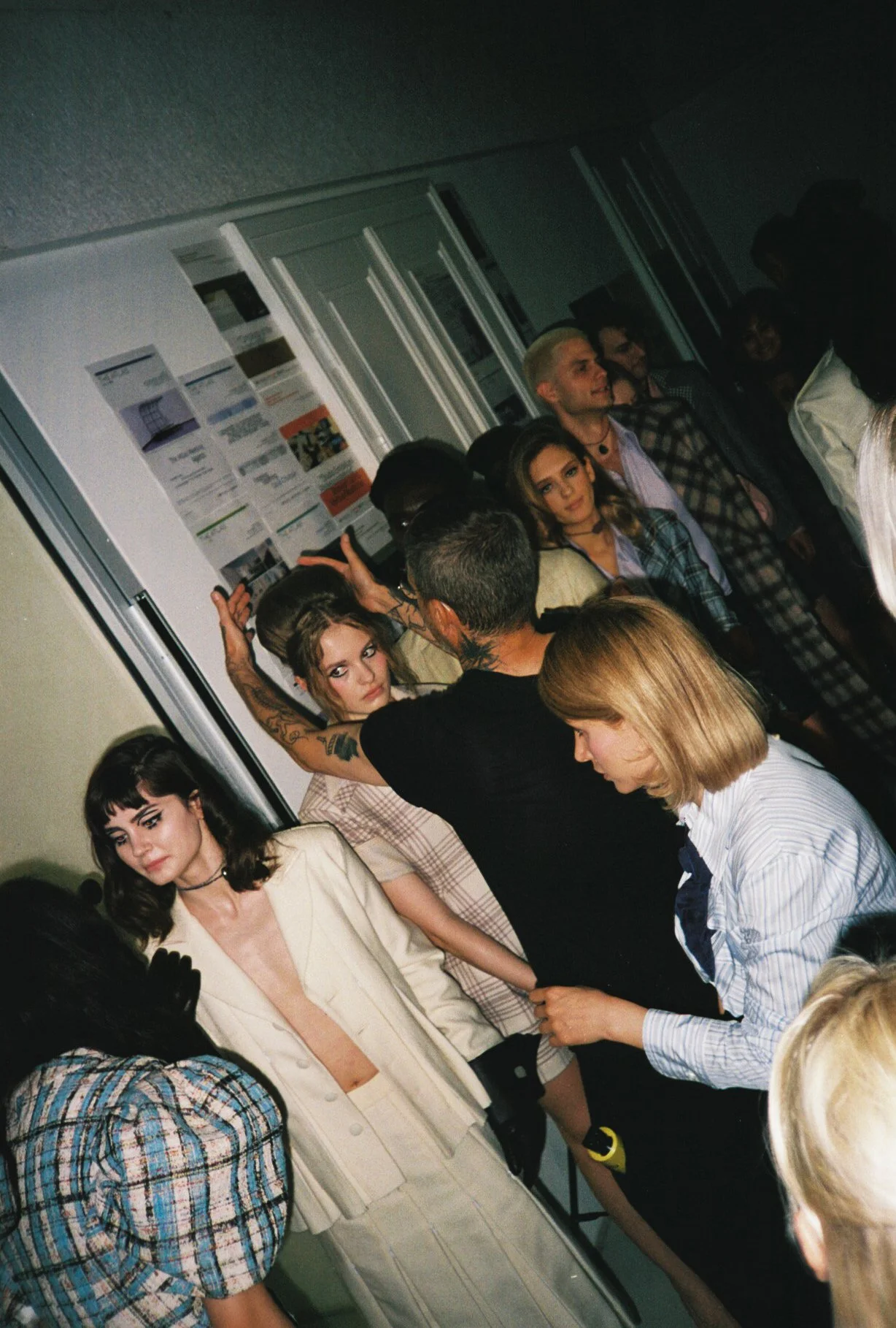 People are gathered indoors, some engaged in conversation, with posters or papers on the wall in the background.