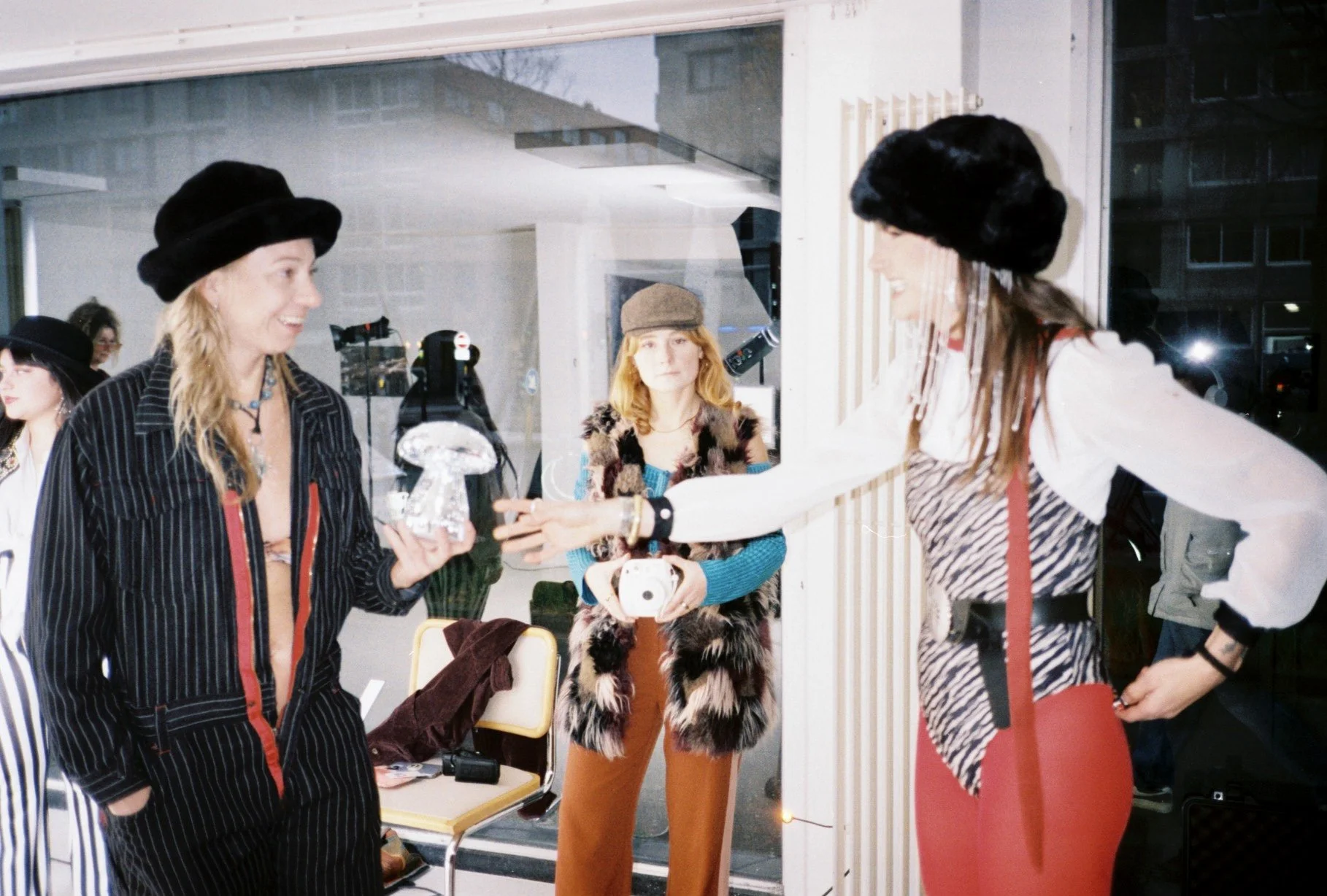 Three women in vintage style clothing at an indoor gathering, one woman receiving an award or gift from another woman.