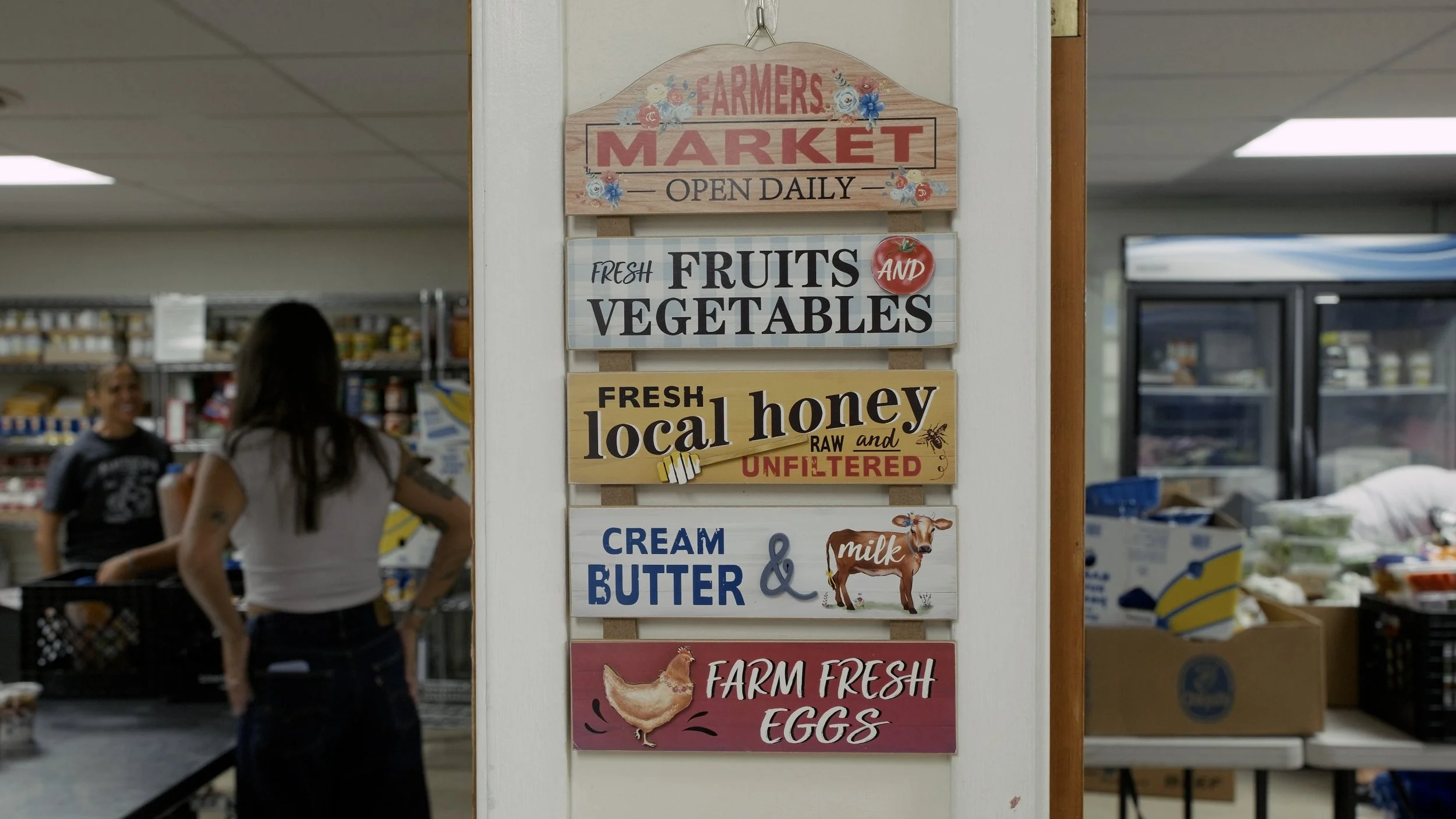 Signboard in a farmer's market advertising fresh fruits and vegetables, local honey, cream, butter, and farm fresh eggs inside a grocery store.
