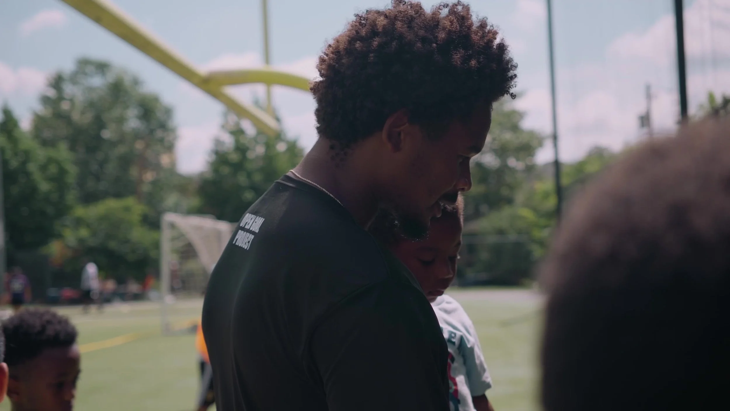 Young man with curly hair bowing his head during an outdoor sports event on a sunny day.