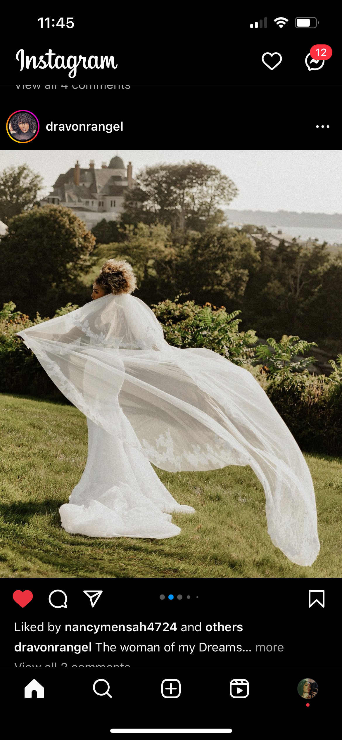 A woman in a wedding dress standing outdoors on a grassy area with trees and bushes in the background, with a large house or castle visible in the distance.