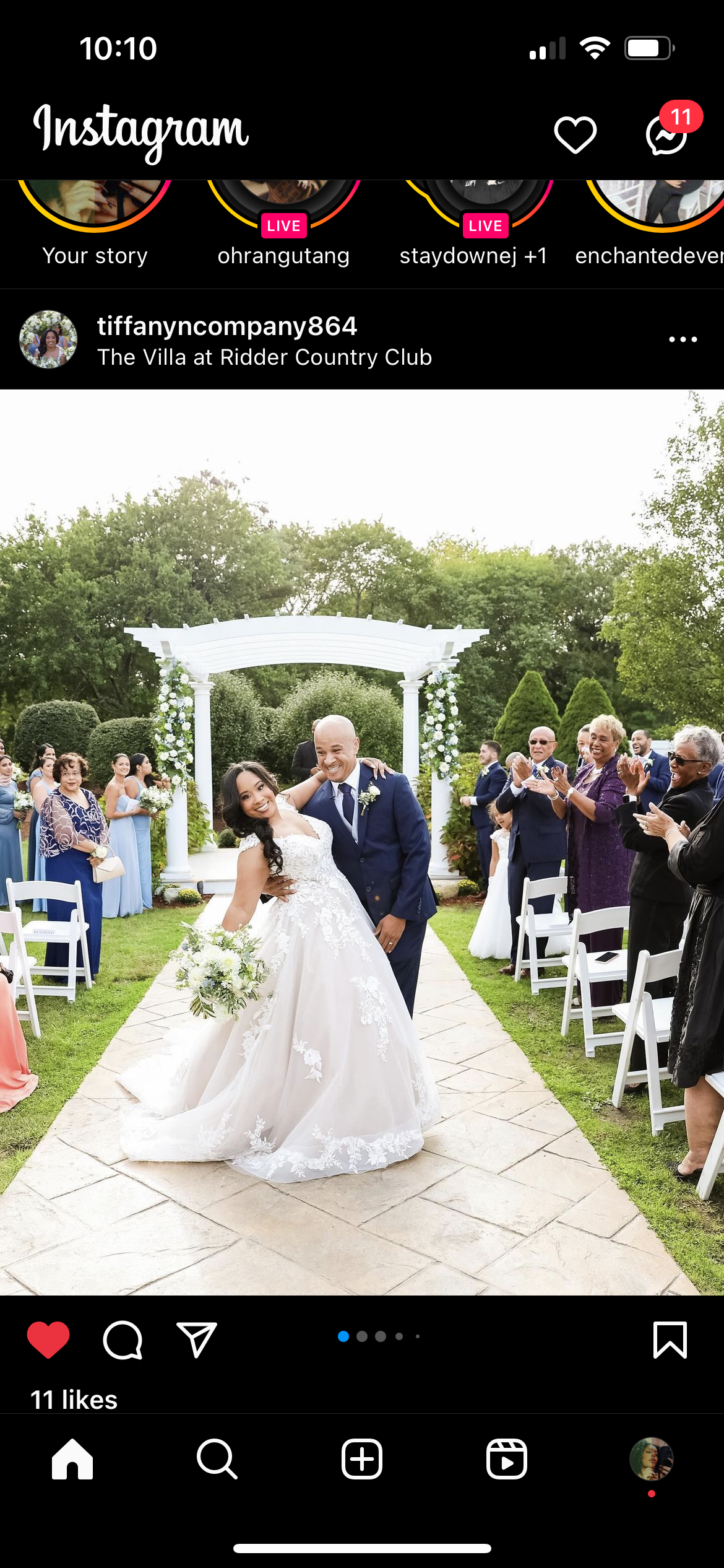 A bride and groom smiling and dancing at their outdoor wedding ceremony, surrounded by family and friends, with a white floral arch in the background.