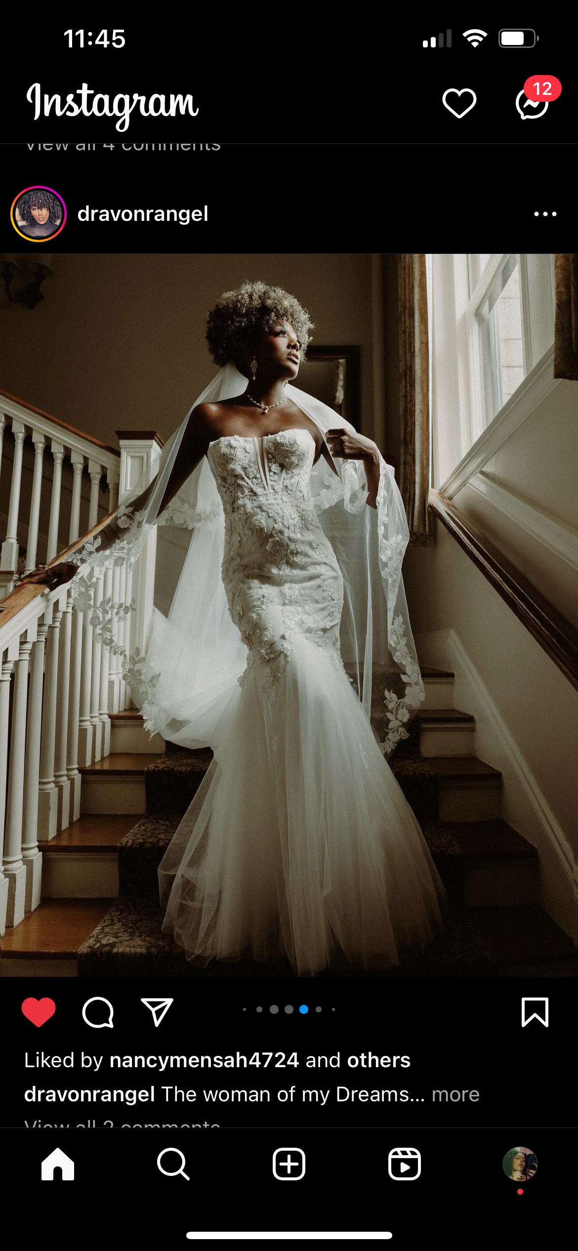 A woman in a wedding dress standing on a staircase, looking out of a window with natural light streaming in, holding a veil