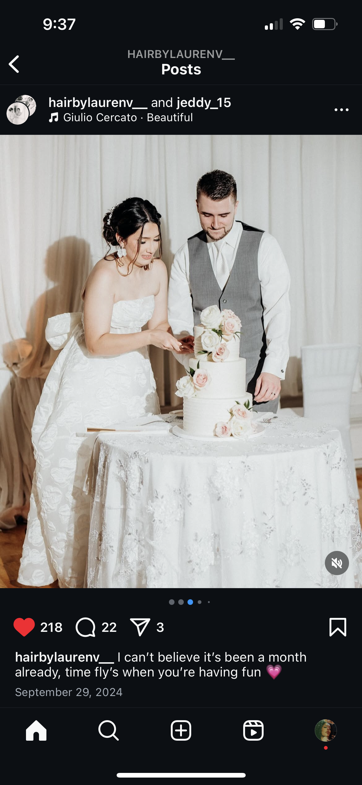 A bride and groom cut a wedding cake together at their reception, with the bride wearing a strapless white wedding gown and the groom in a grey vest and white shirt, standing in front of white curtains.
