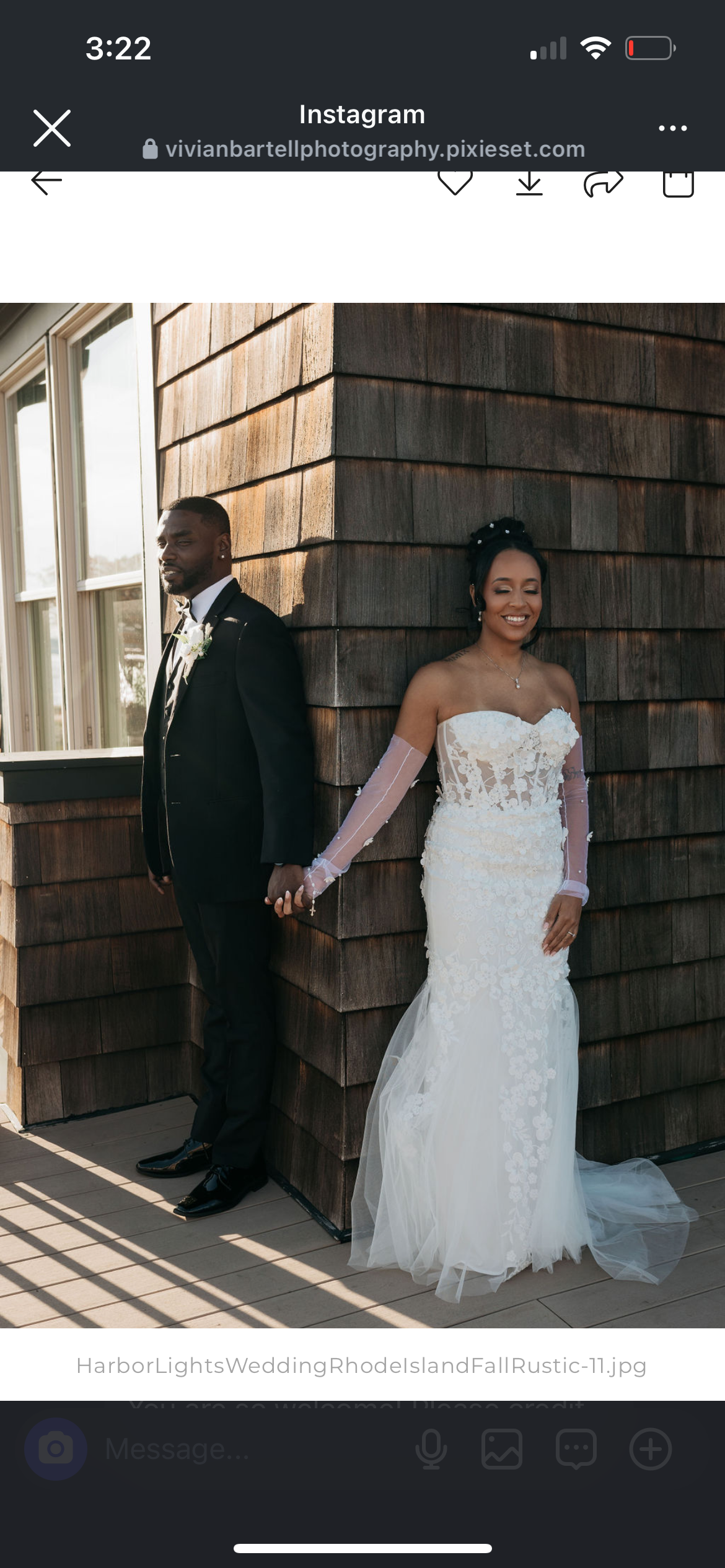 A bride and groom standing back-to-back outdoors, holding hands, near a wooden wall and window, with the bride wearing a white wedding dress and the groom in a black tuxedo.