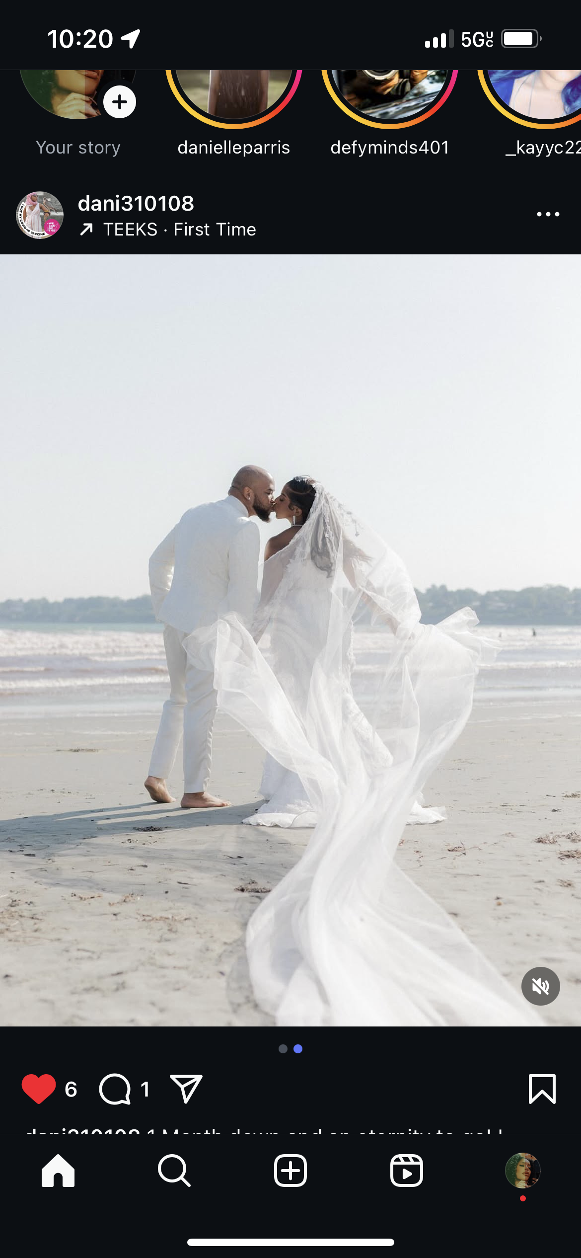 A bride and groom sharing a kiss on a beach, with the bride wearing a white wedding dress and veil, and the groom in a white suit, both barefoot on the sand.