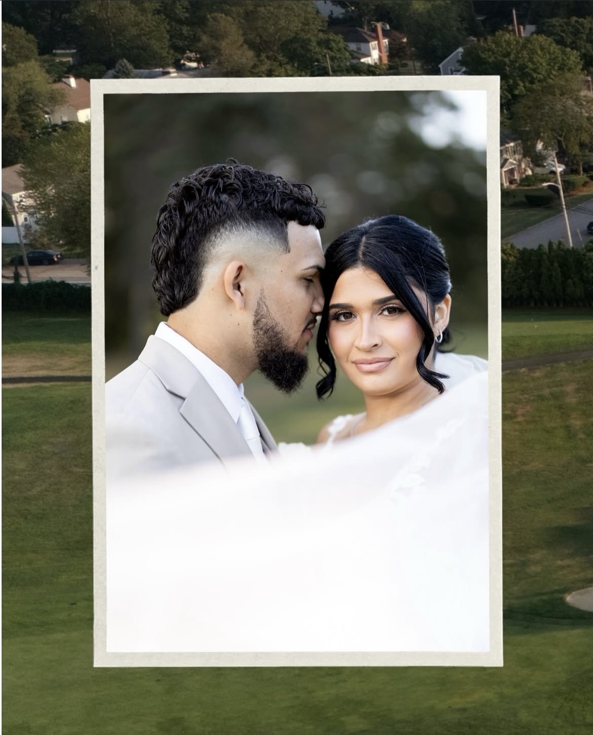 A young couple in wedding attire, the man with styled dark hair and a beard, and the woman with dark hair styled in waves, sharing a close, intimate moment outdoors with a blurred green background.