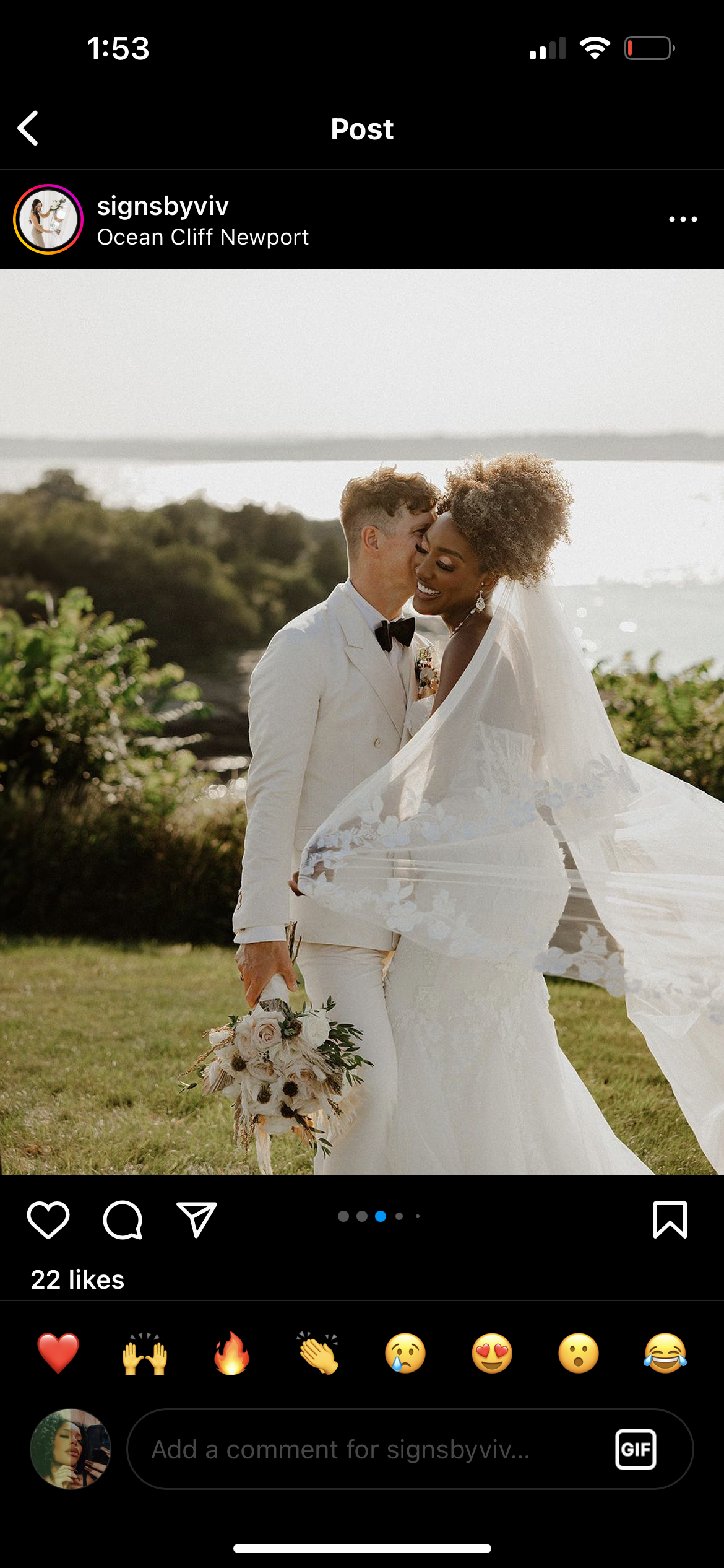 A bride and groom share a joyful moment outdoors on their wedding day, with the bride wearing a white wedding dress and veil, and the groom in a white tuxedo with a black bow tie, standing by the coast in Newport with greenery and water in the backgr