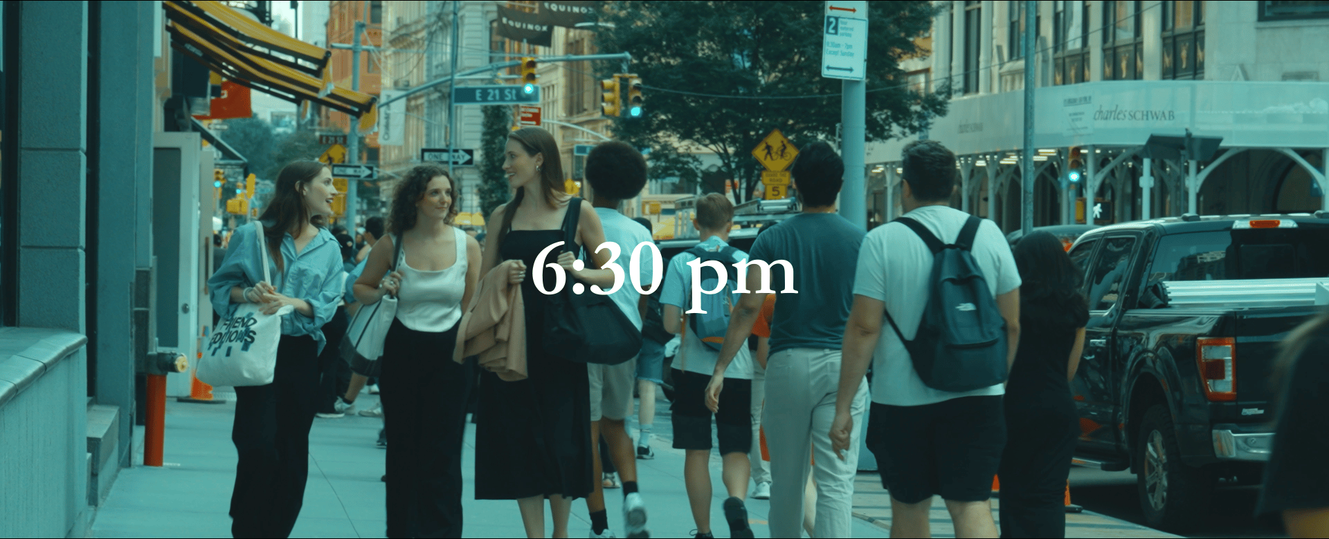 A busy New York City sidewalk scene with people walking and talking, tall buildings, yellow traffic lights, and street signs. The time overlay shows 6:30 pm.