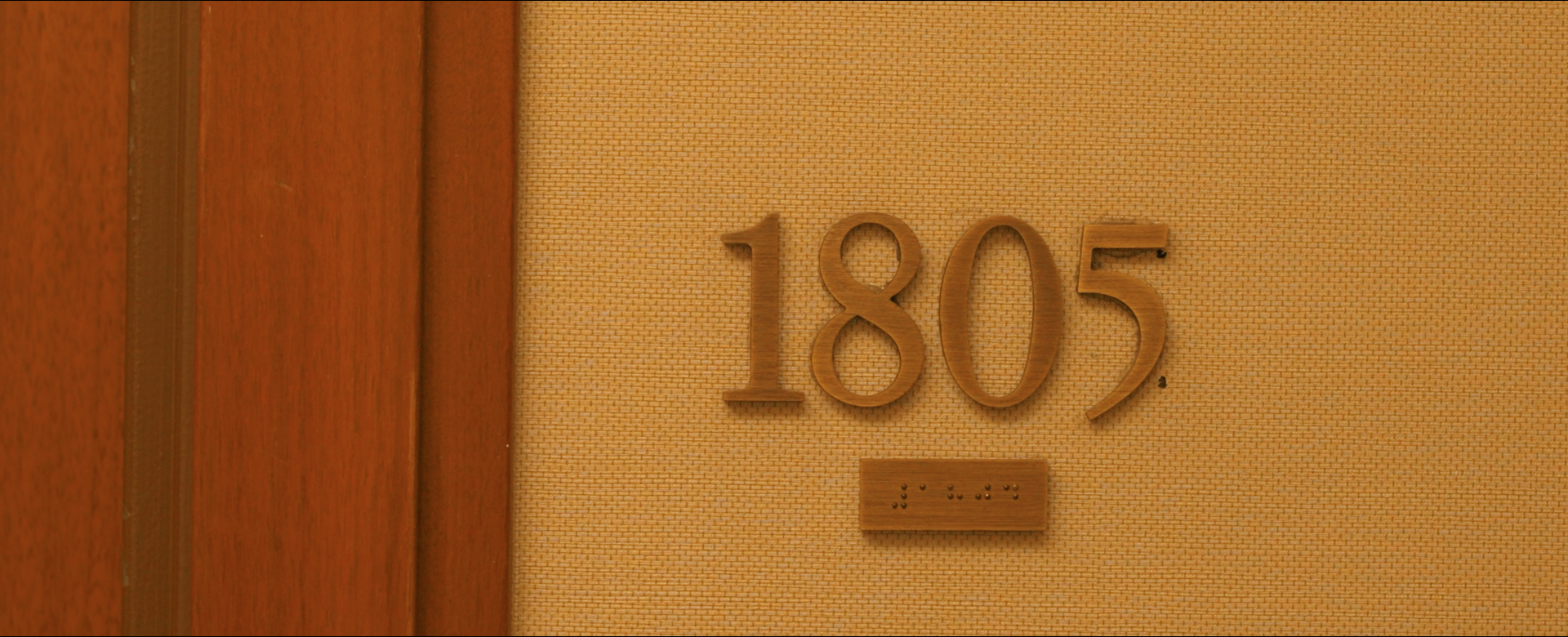 Wooden house number plaque with the number 1805 mounted on a textured beige wall.