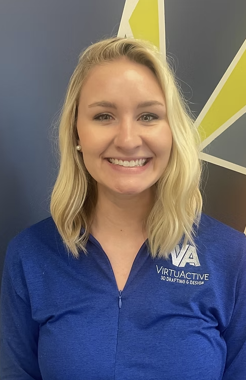 Young woman with blonde hair smiling, wearing a blue jacket with 'VirtuActive 3D Drafting & Design' logo, standing in front of a gray wall with yellow and white geometric design.