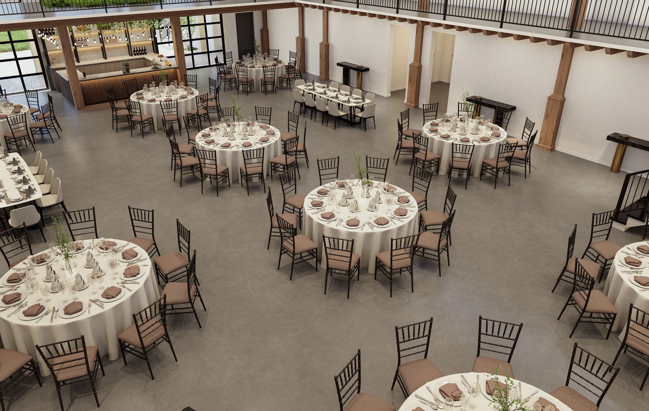 Banquet hall with round tables set for a formal event, each with white tablecloths, tableware, napkins, and small centerpieces, surrounded by black chairs with brown cushions, and a bar area in the background.