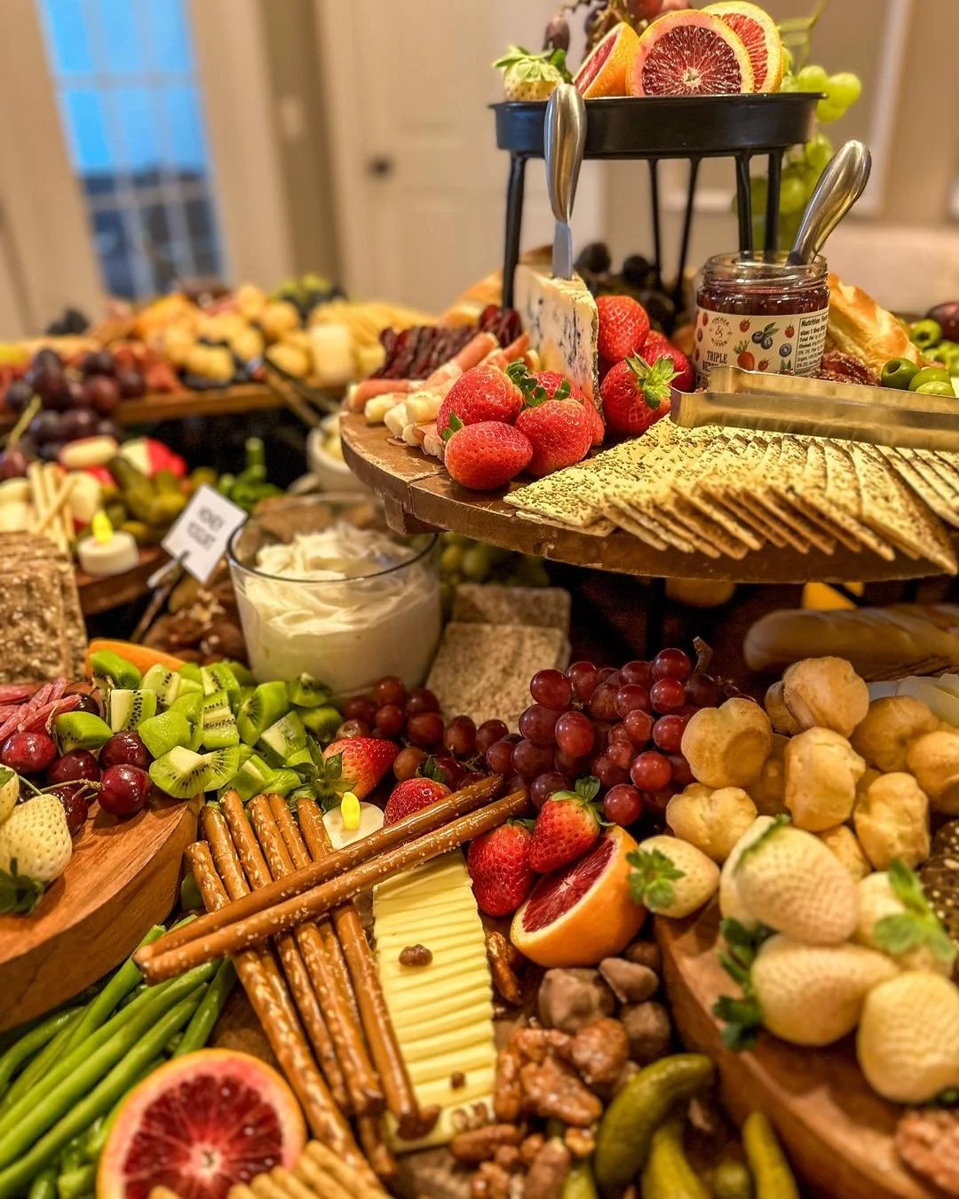 A colorful assortment of fresh fruits including strawberries, grapes, kiwi, citrus slices, and more, arranged on a multi-tiered serving platter with crackers and cheese.