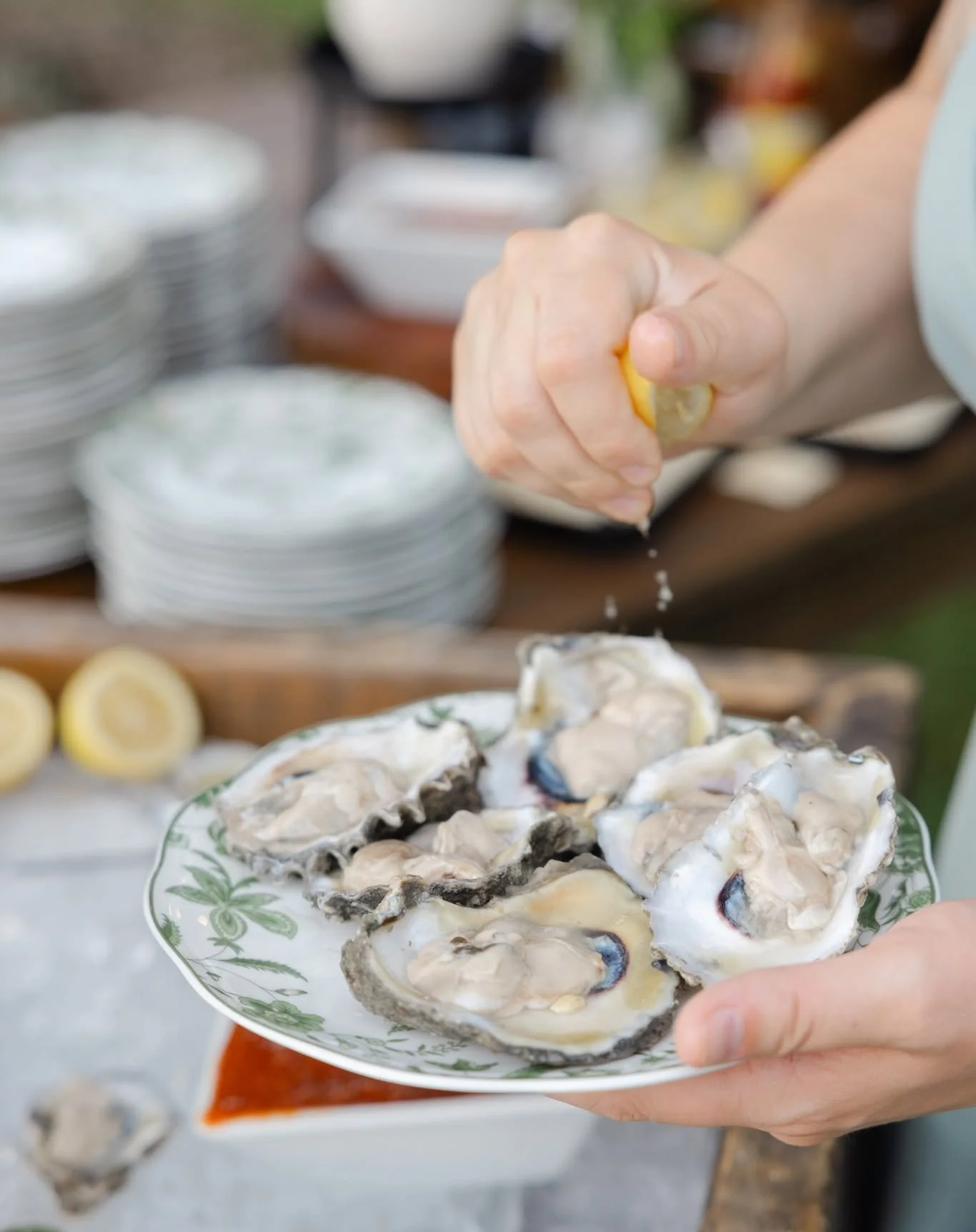 Person squeezing lemon over fresh oysters on a plate.