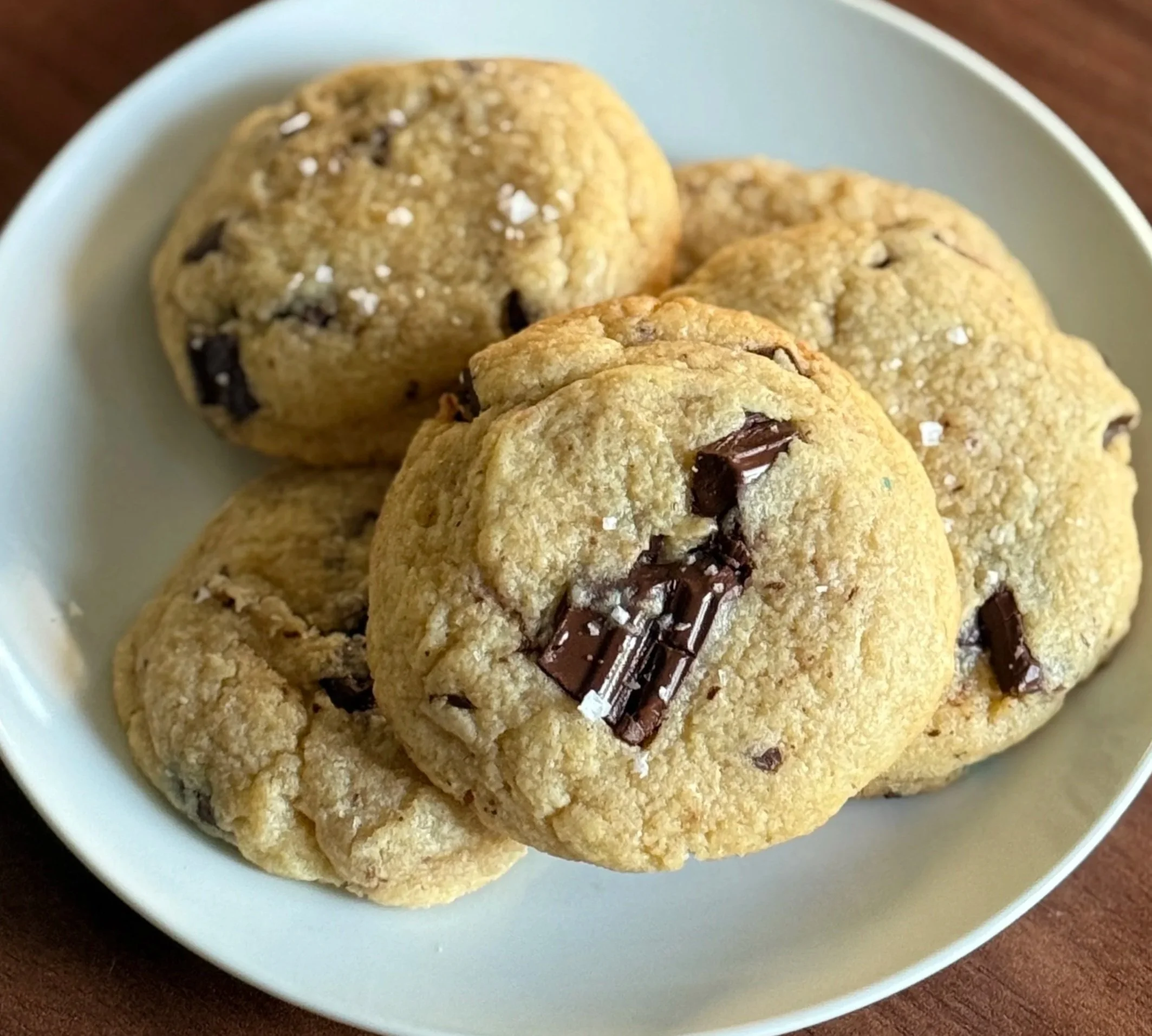 A white bowl filled with chocolate chunk cookies on a wooden surface.
