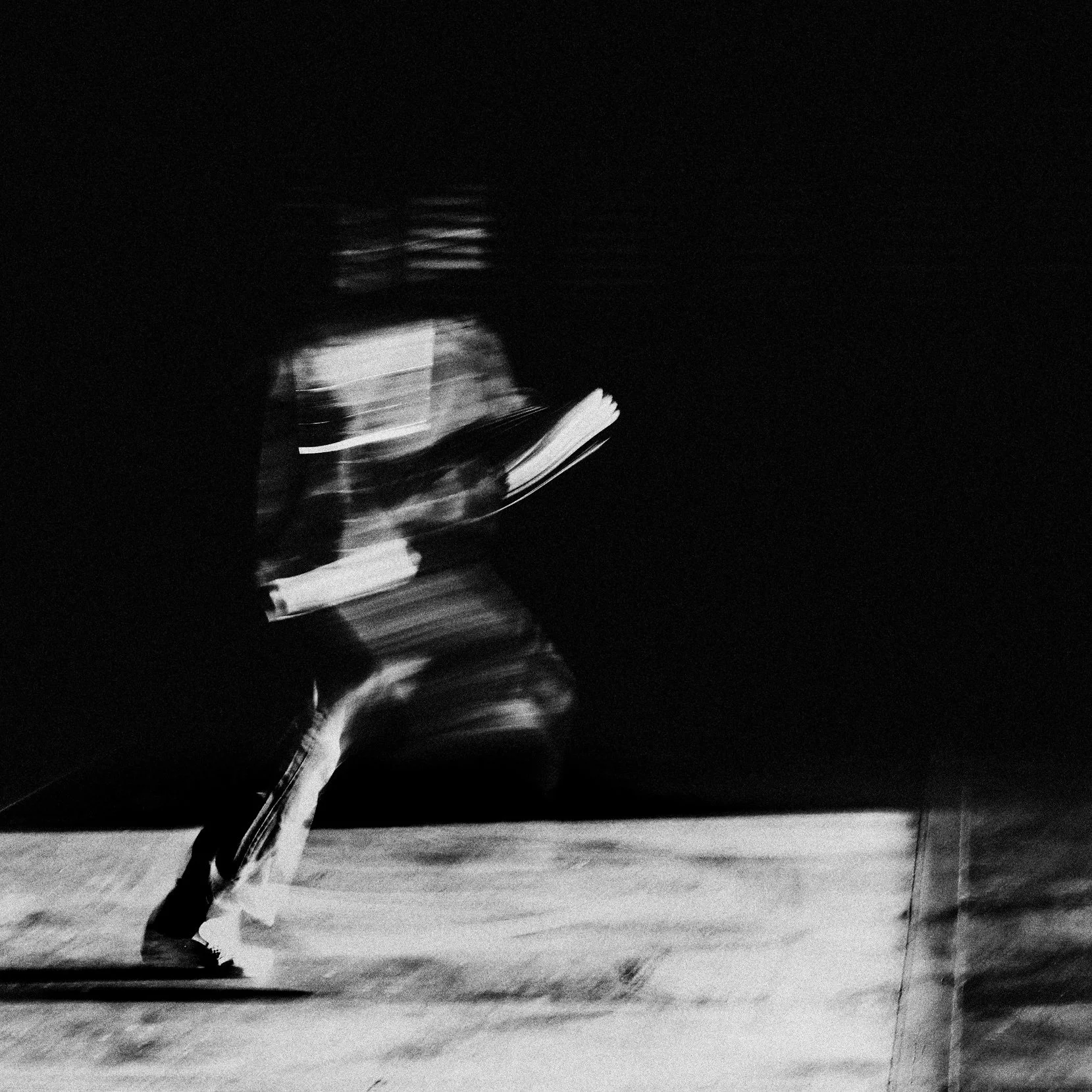 A black and white photo of a skateboarder in motion, captured with a slow shutter speed, creating a blurred effect.