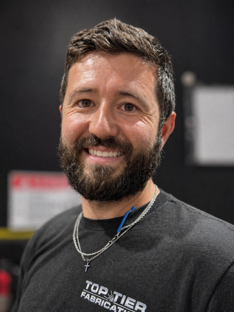 Ty is a white man with a full beard, smiling & looking at the camera