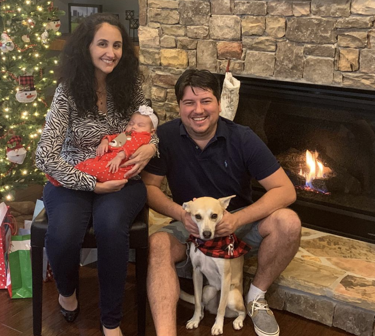 A smiling woman with short black hair, wearing a blue top, standing among green plants in a bright indoor environment.