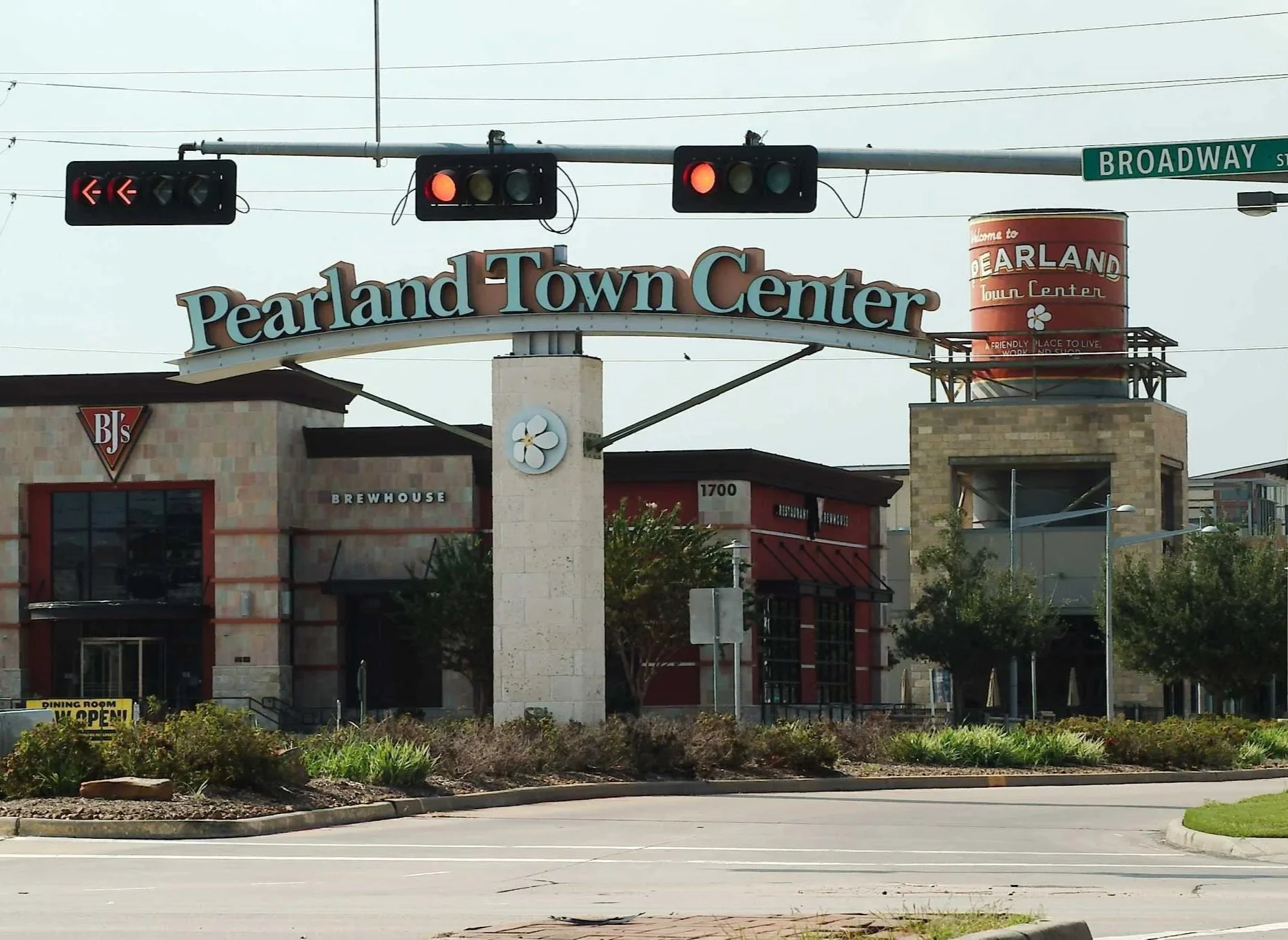 Sign for Pearland Town Center shopping mall with traffic lights, trees, buildings, and a street at the entrance.