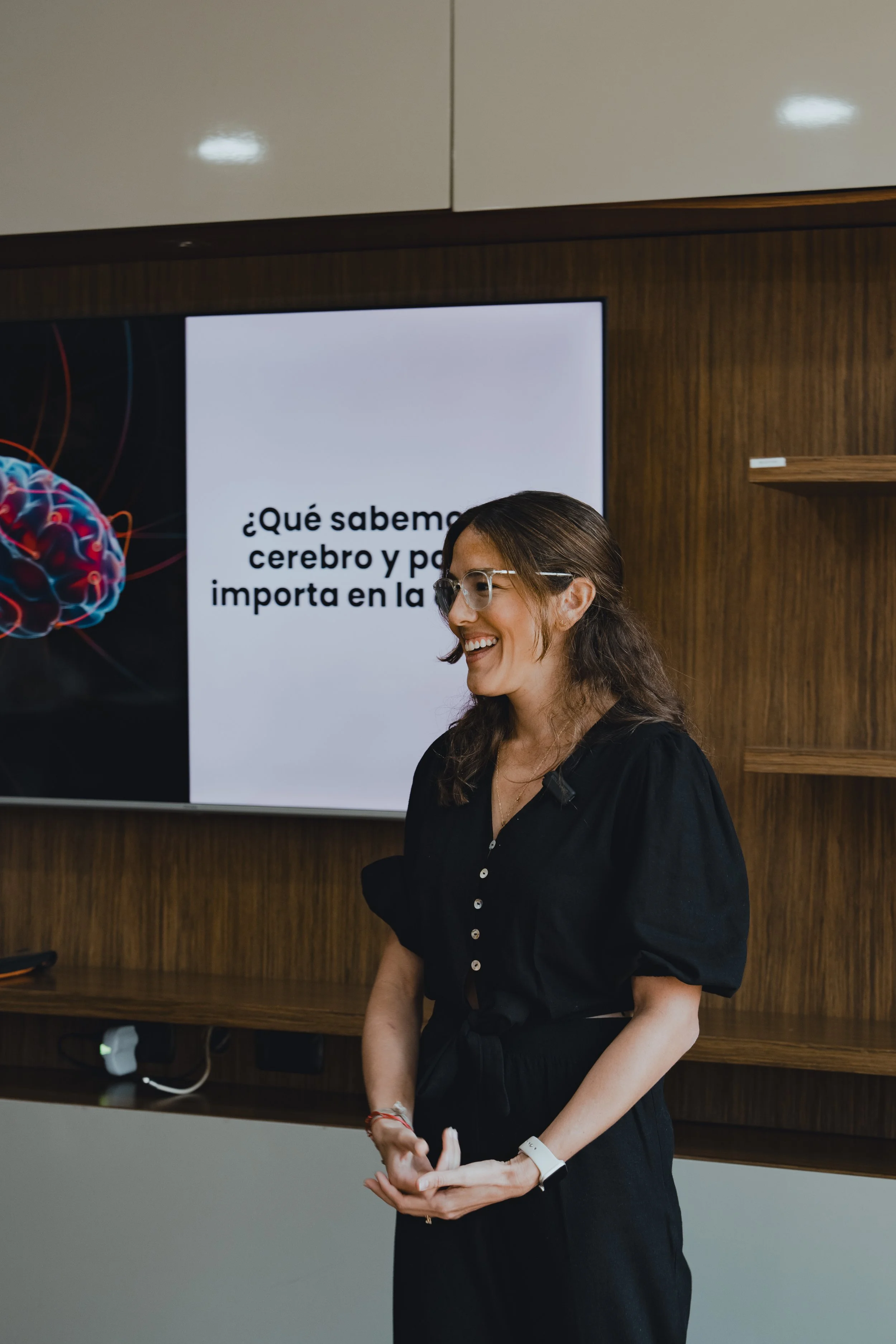 Mujer dando una charla en una sala de conferencias, con una pantalla que muestra un título en español sobre el cerebro y su funcionamiento.