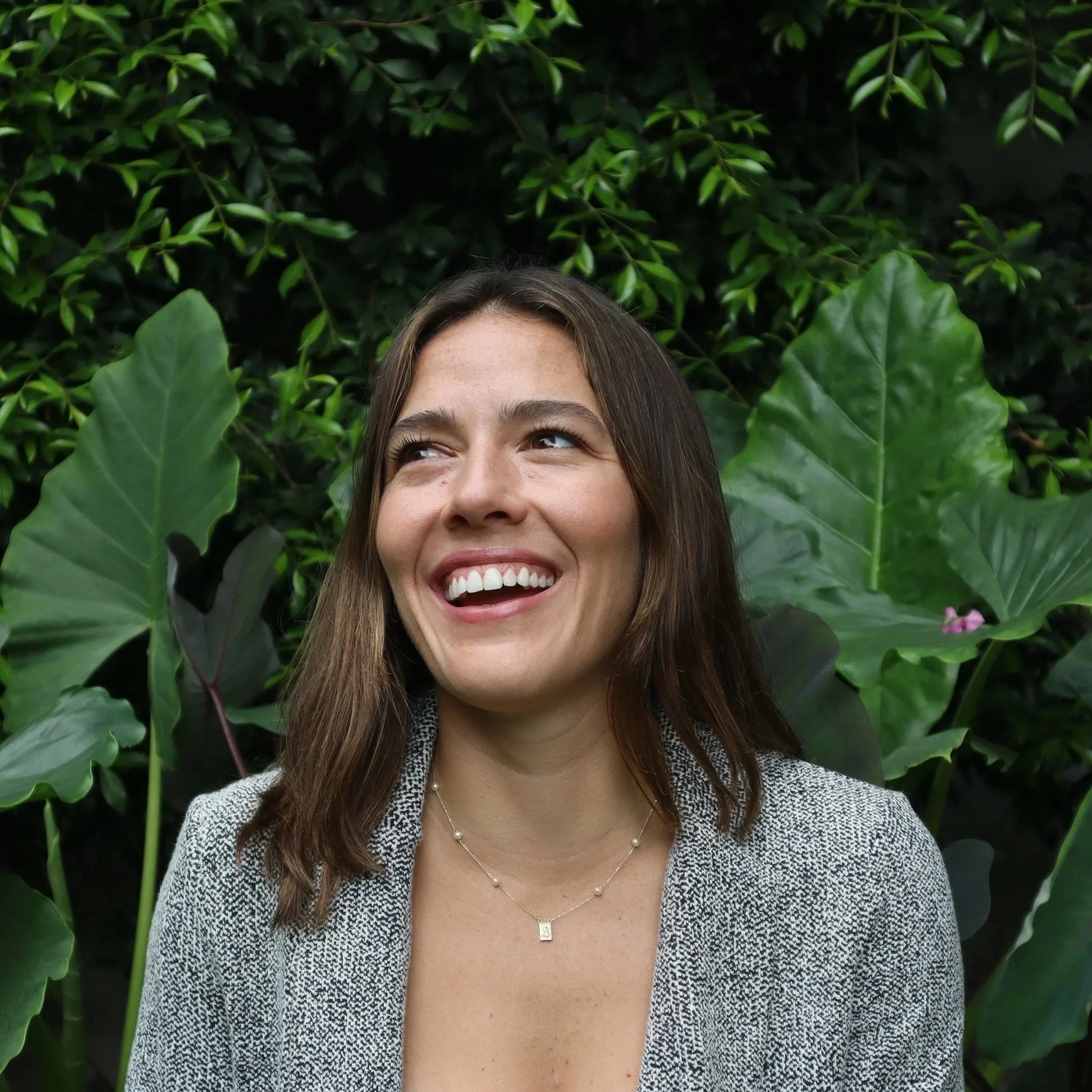 Retrato de una mujer sonriendo, rodeada de plantas verdes grandes.