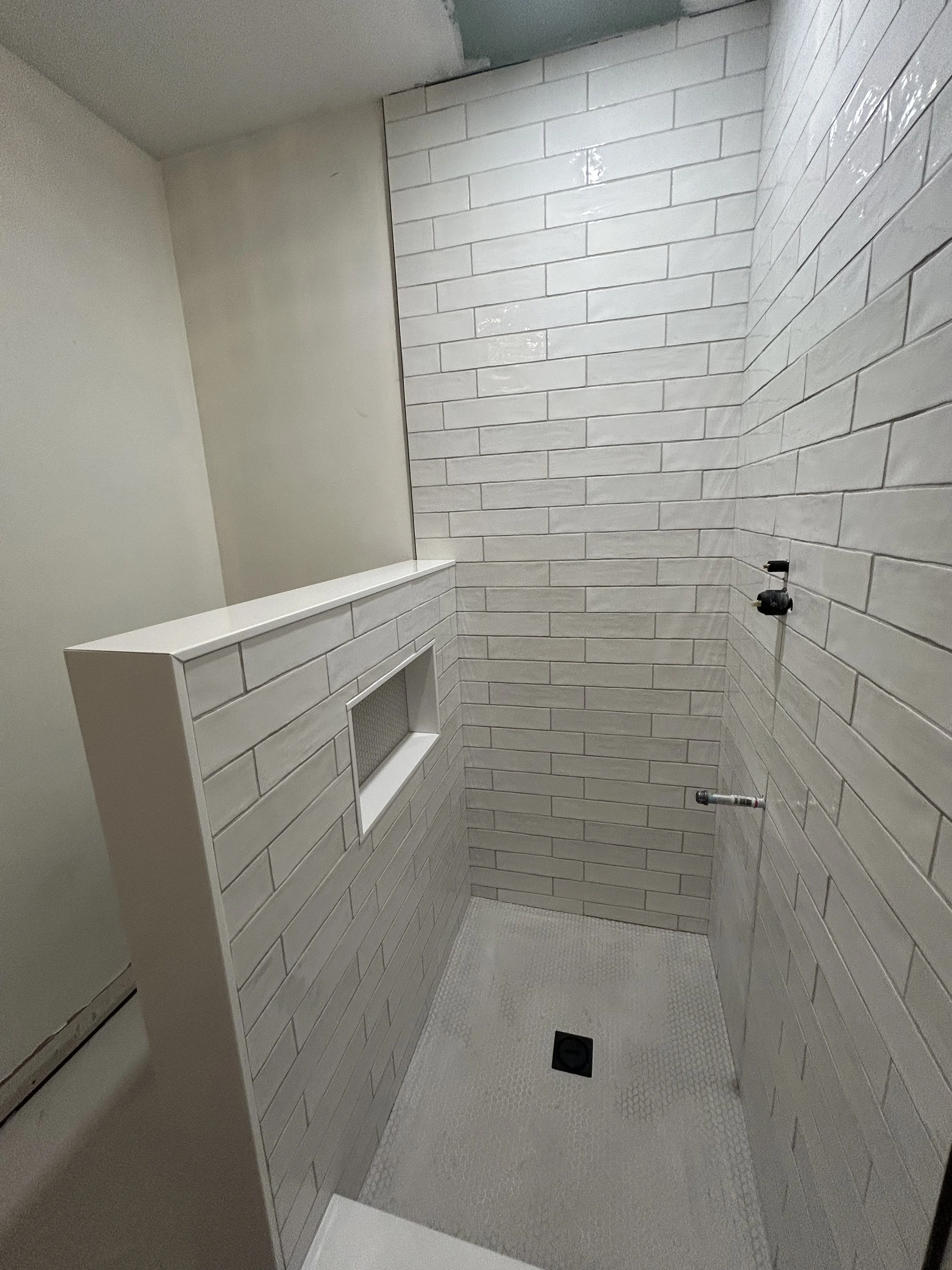 A partially tiled shower with white subway tiles on the walls, a built-in niche, and a textured floor with a drain.