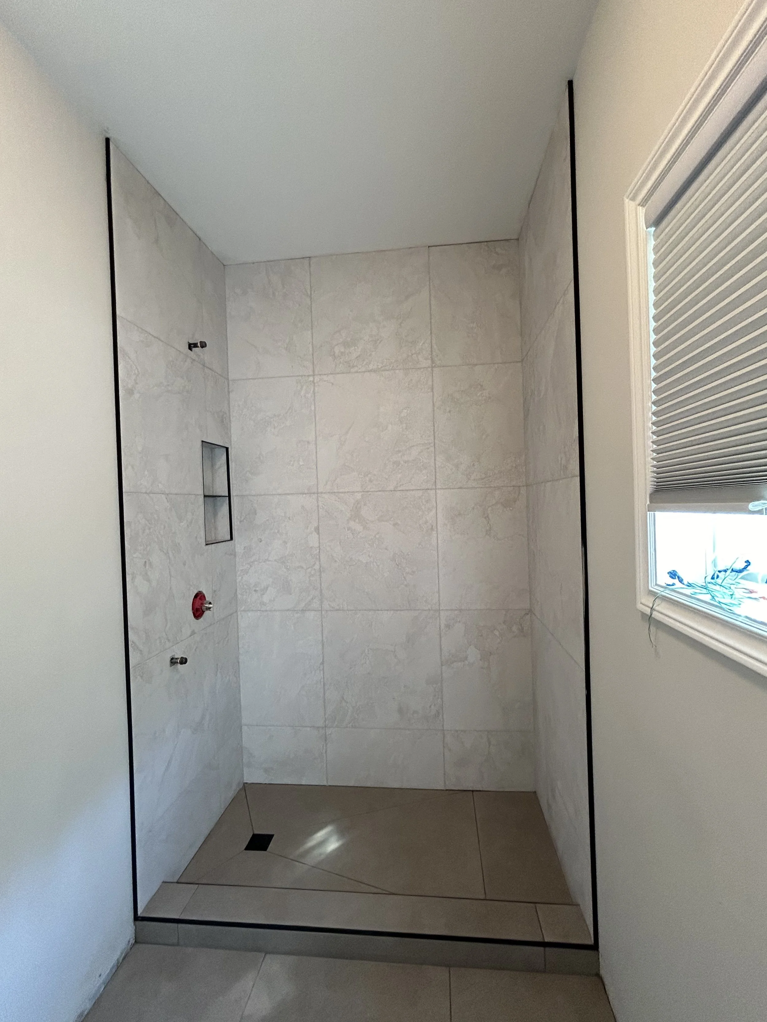 Empty shower with tiled walls, small built-in shelf, and a window with blinds