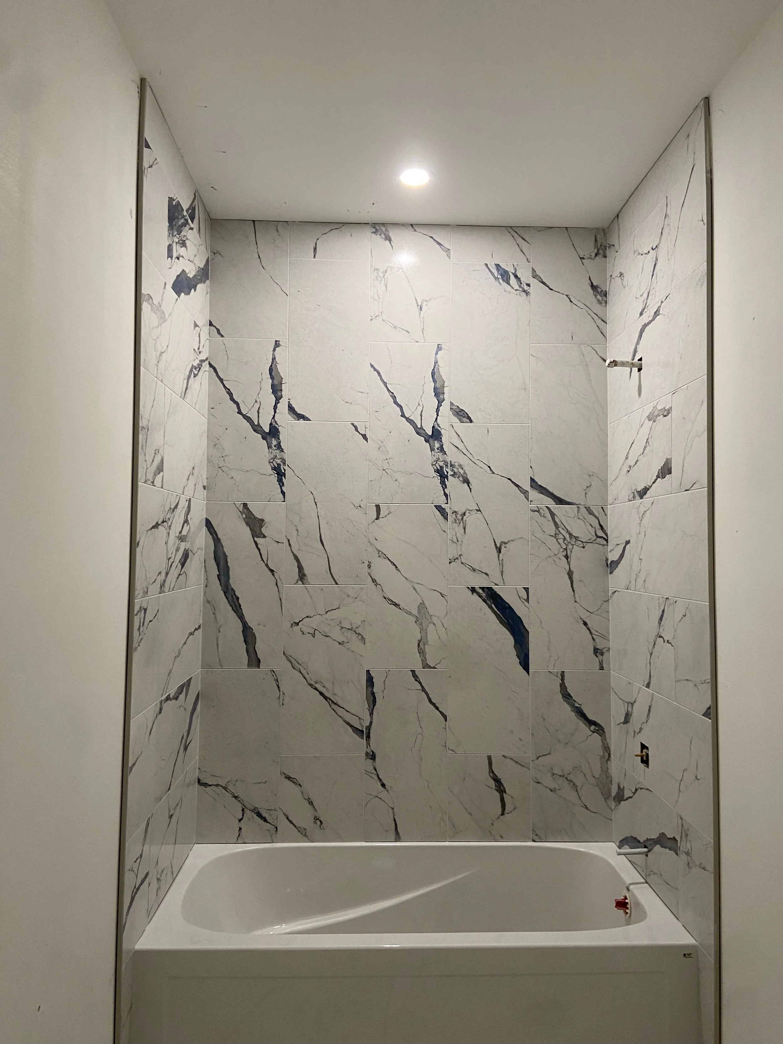 Bathroom with marble-tiled wall, bathtub, ceiling light, and partially visible fixtures.