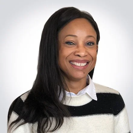 A woman with long black hair smiling, wearing a white shirt and a black and white striped sweater, posing against a plain background.