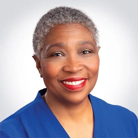 A smiling woman with short gray hair wearing a blue top against a white background.