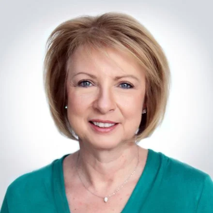 A middle-aged woman with short, blonde hair smiling against a plain white background.