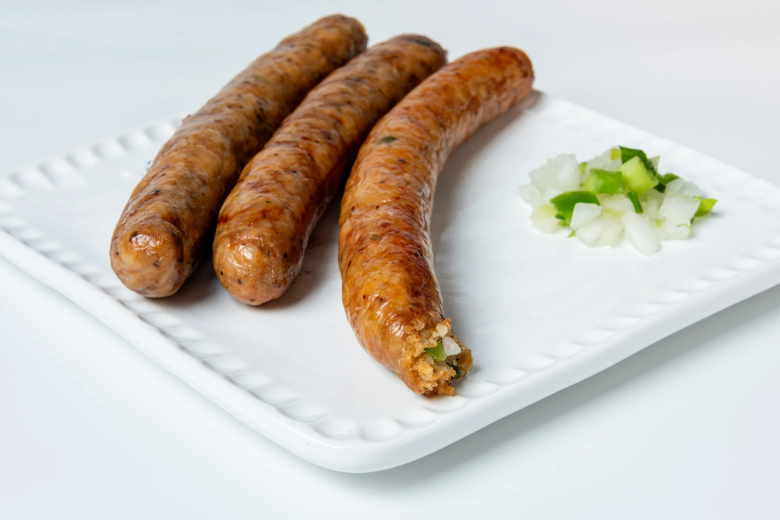 Three cooked boudin links with chopped onions and green peppers on a white rectangular plate.