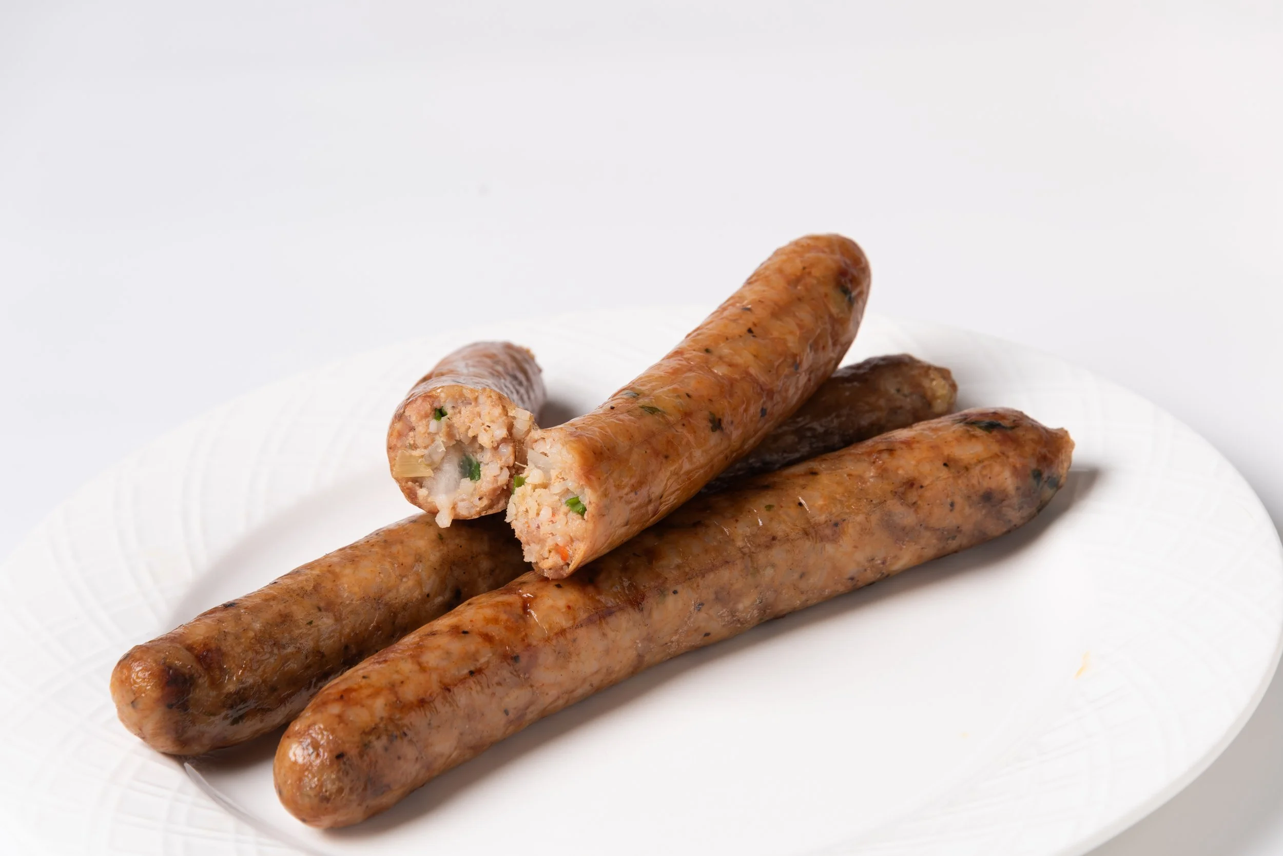 Three grilled boudin links on a white plate, one sliced open to reveal the seasoned meat inside.