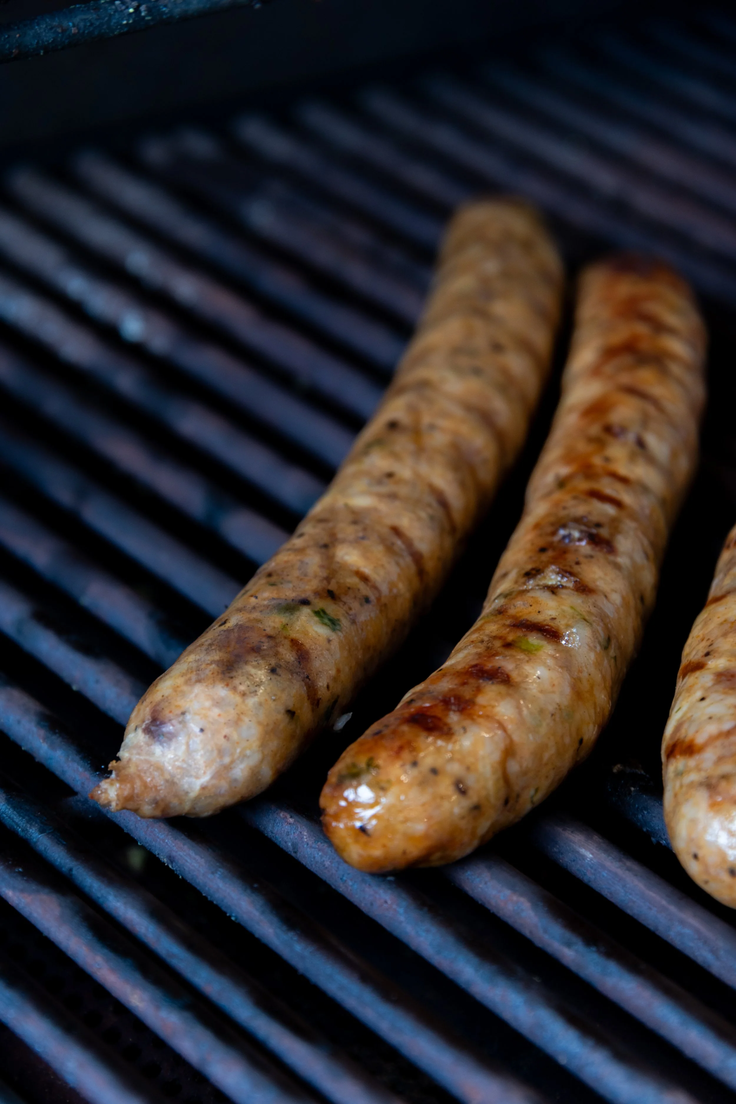 Two boudin grilling on a barbecue grill with visible grill marks.