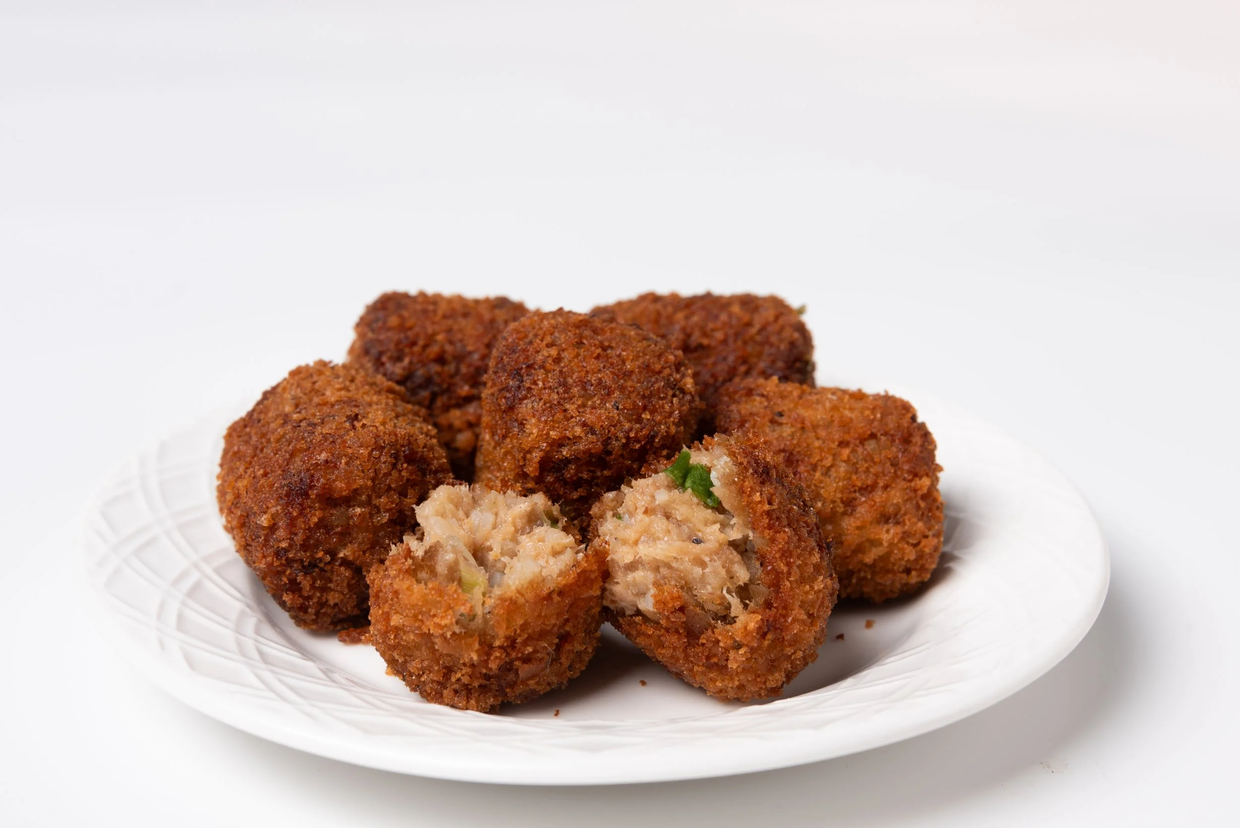 Plate of breaded, deep-fried boudin balls with one boudin ball cut open showing a meat and vegetable filling.