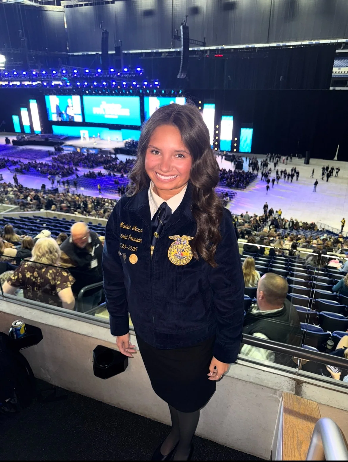Madelin Garcia stands before the National FFA convention center, smiling and wearing a blue corduroy FFA jacket. 