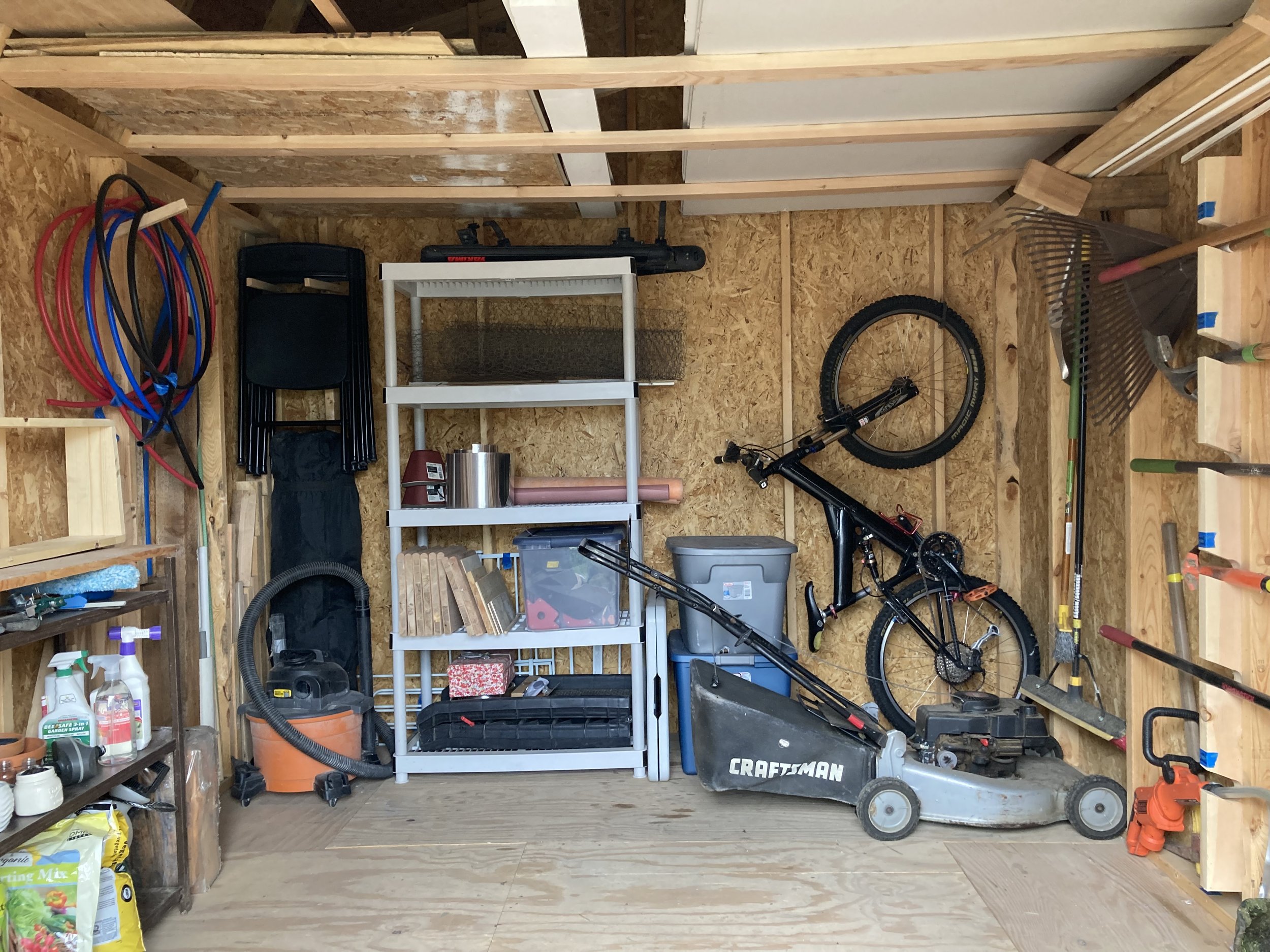Organized shed with a lawn mower, shelves, a bike, and gardening stuff